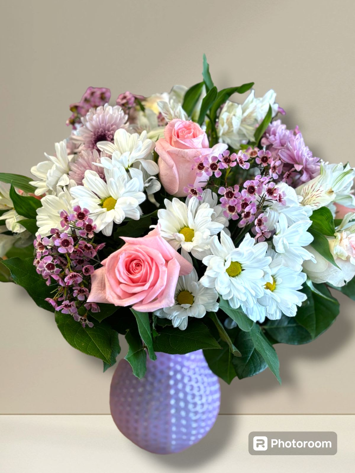 Pastel Blossom Dream - You could describe it as:  "Embrace the elegance of spring with our  Pastel Blossom Dream arrangement. Delicate white daisies and pink roses intertwine with vibrant purple wax flowers.  This enchanting bouquet captures the essence of beauty and serenity, perfect for celebrating the special moments with your loved ones."