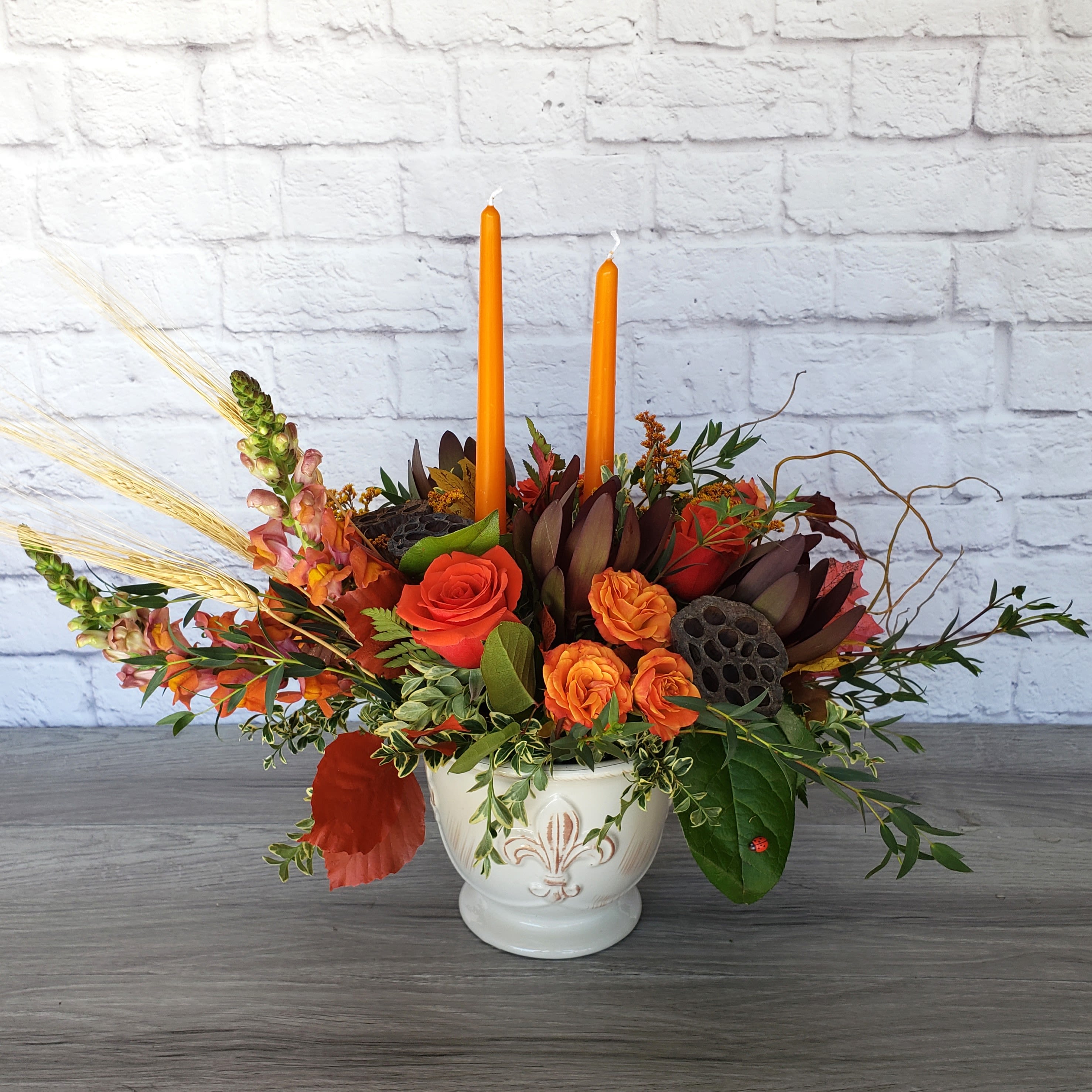 Fall Blessings Centerpiece - Inspired by our November special, Fall Blessings Centerpiece is a larger and longer bouquet featuring  roses, spray roses, safari sunset, snap dragons, curly willow, solidago, eucalyptus, lotus pods and dried wheat all within a hand-crafted ceramic pot. This centerpiece is A Ladybug Floral exclusive bouquet made with your family gathering in mind.  Orientation: all around 18”H X 28"W X14"D 