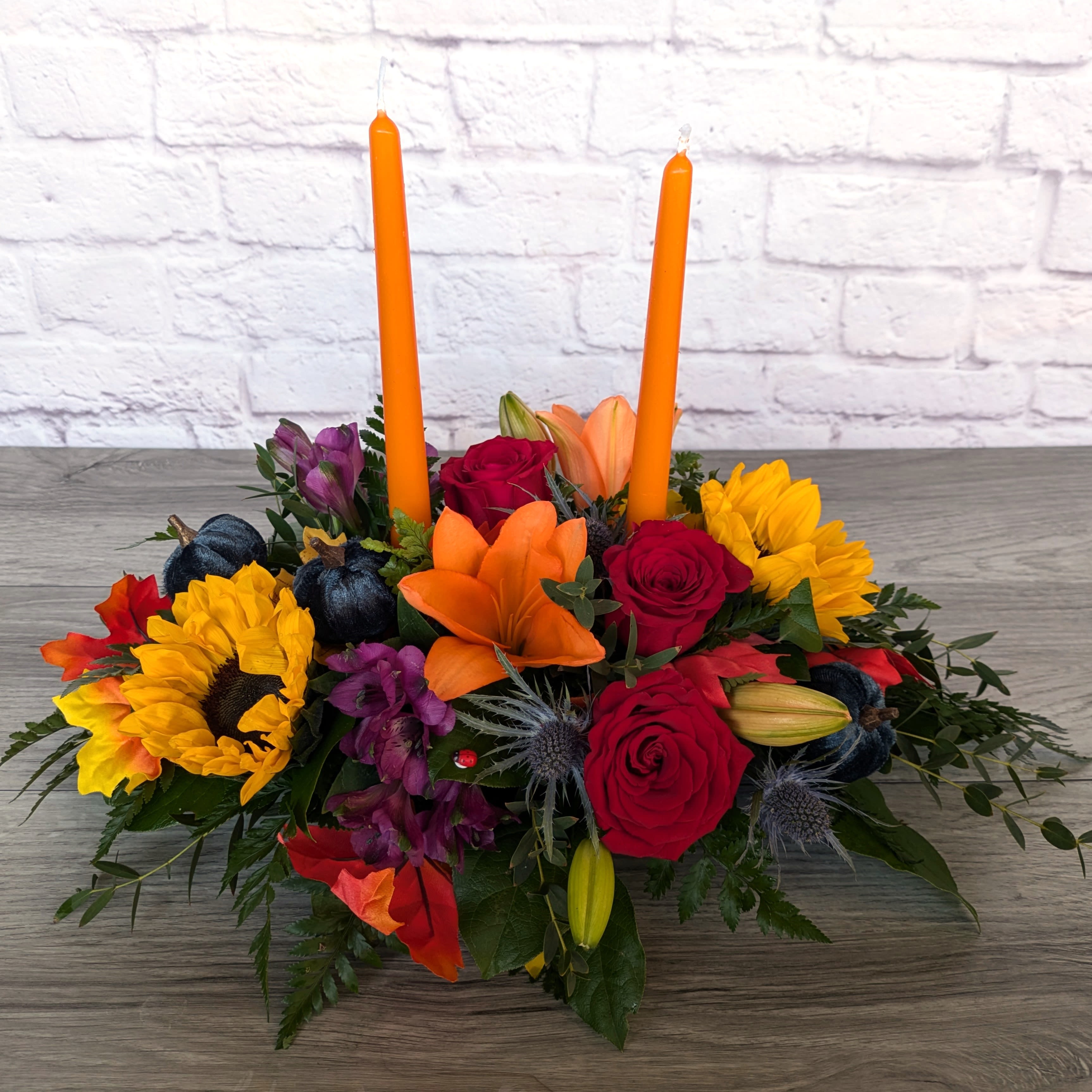Jewels of Autumn Centerpiece  - Jewels of Autumn Centerpiece is A Ladybug Floral exclusive bouquet. This jewel toned centerpiece features lilies, sunflowers, roses, alstroemeria, thistle, and mini velvet pumpkins.  All Around Orientation 6"H without candle 13.5" with candle X 20"W 