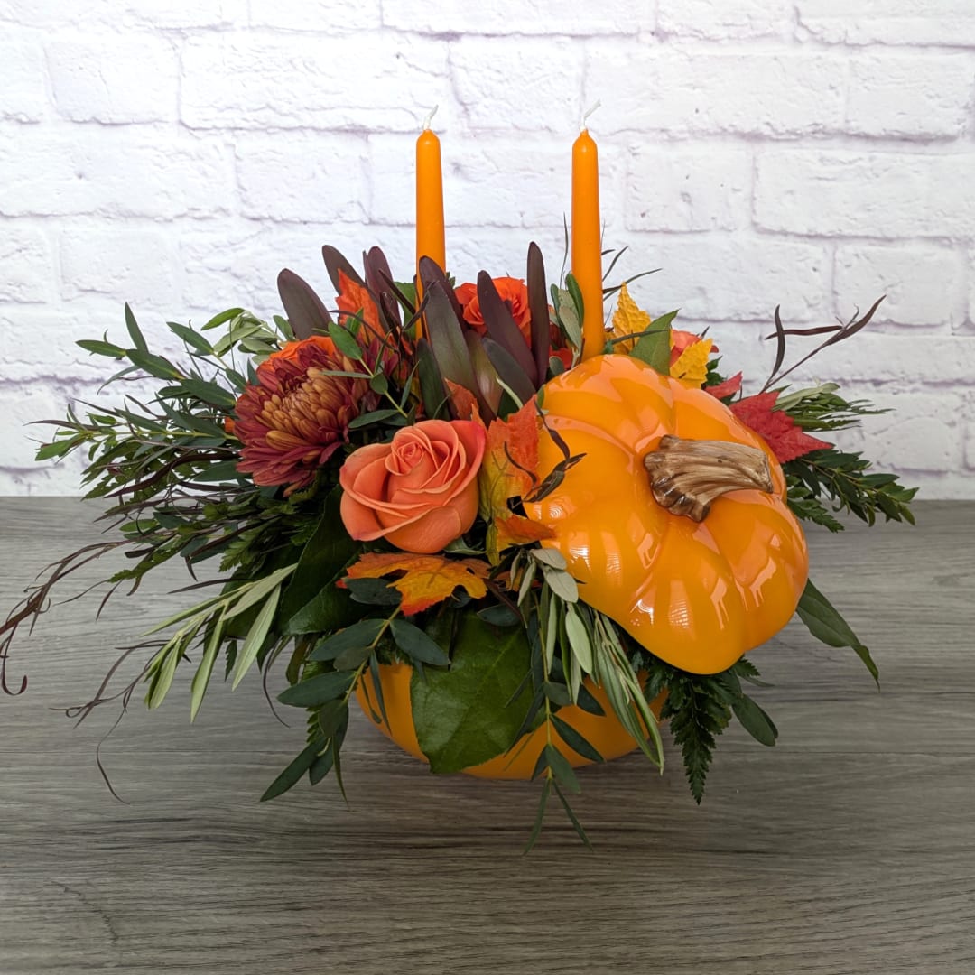 Orange pumpkin centerpiece with roses, mums, and two taper candles