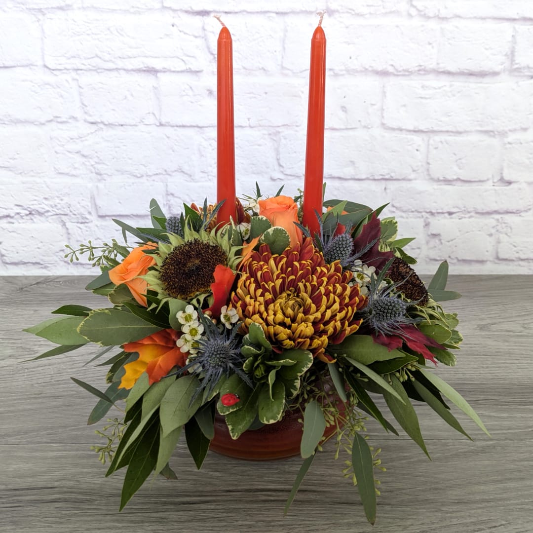 Orange and burgundy floral centerpiece with two tall red candles