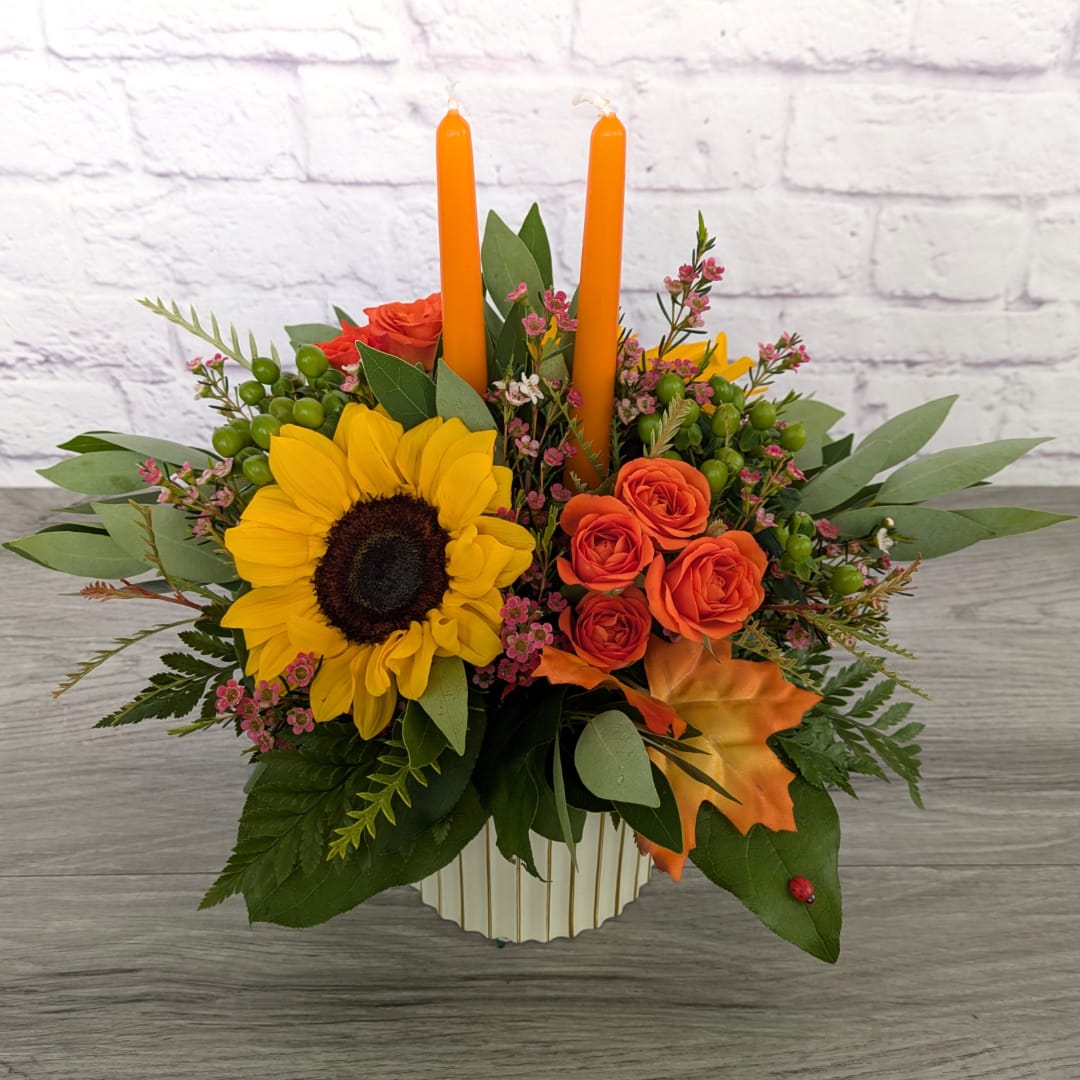 Sunflower and orange rose arrangement with two orange candles in a vase