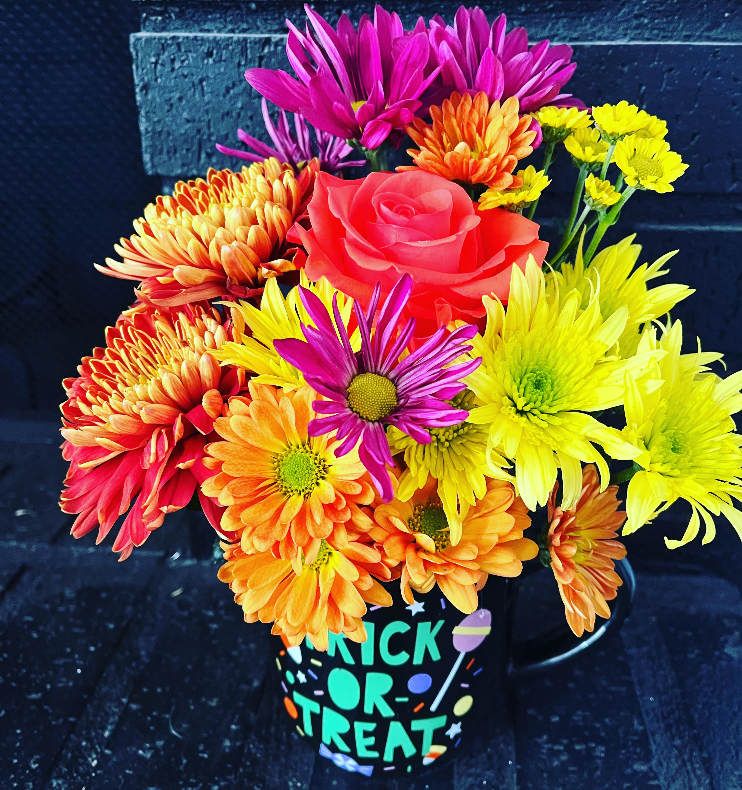 Colorful bouquet of daisies and a rose in a Halloween mug