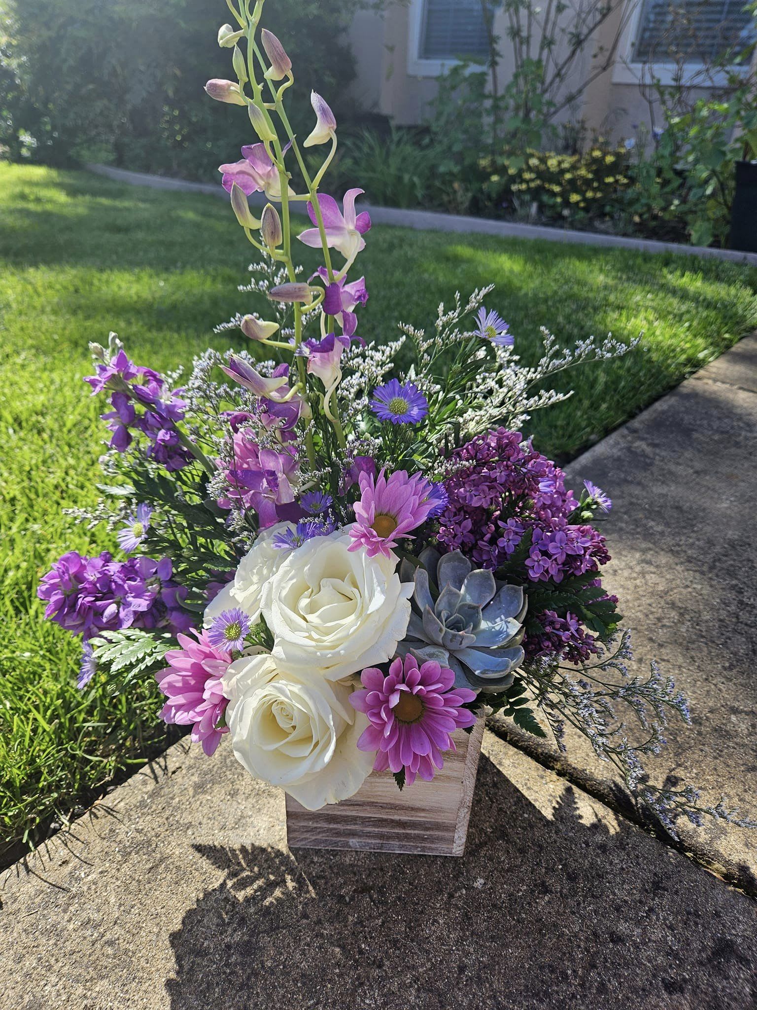 Purple and white floral arrangement in a wooden box with a succulent