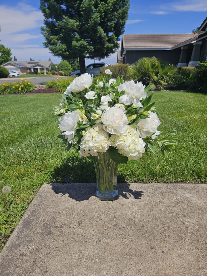 White floral arrangement in a clear glass vase on a sidewalk