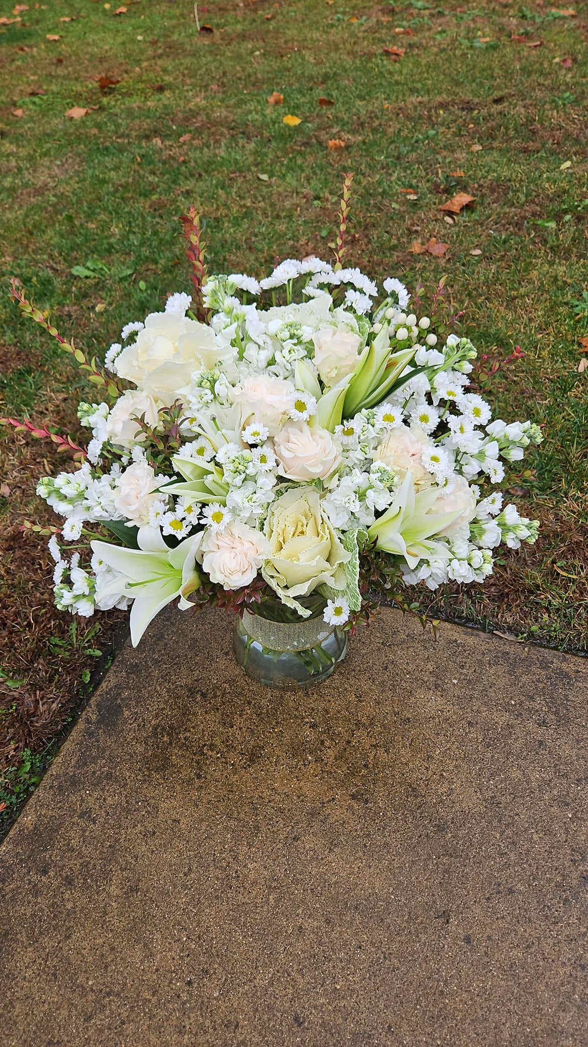 White floral arrangement in a clear glass vase on a sidewalk