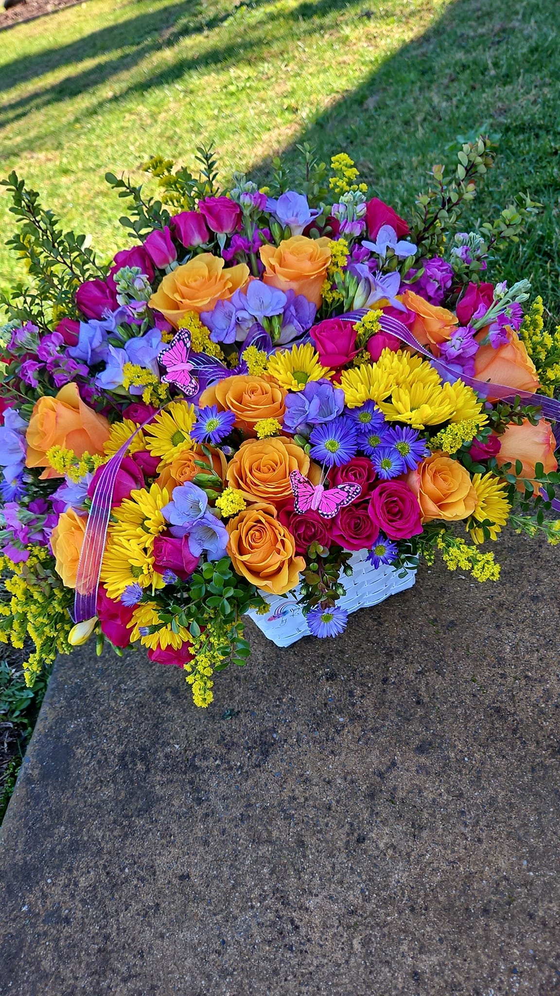 Colorful bouquet of roses, daisies, and purple blooms in a white basket