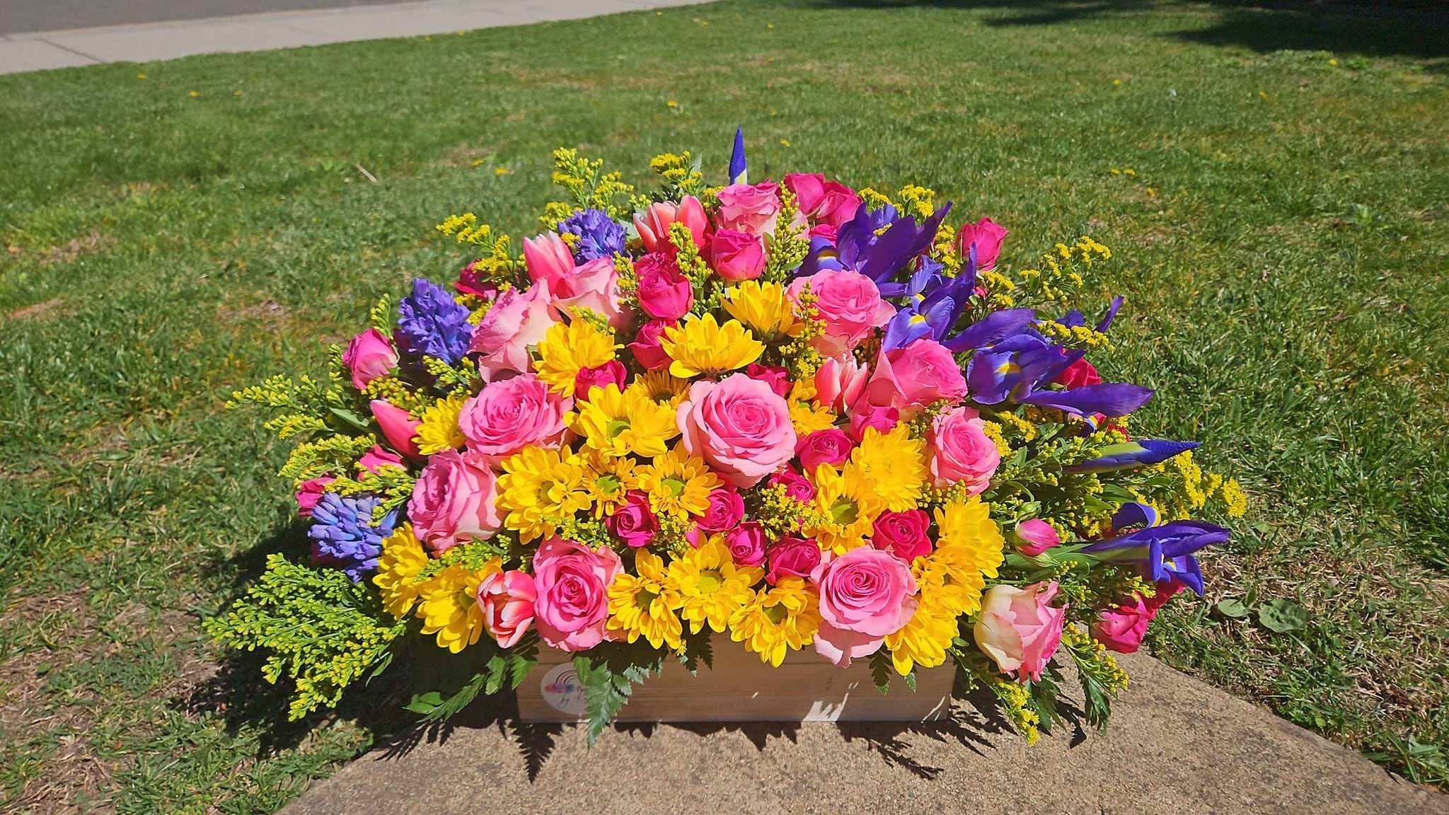 Bright mixed bouquet of pink roses, yellow daisies, and purple irises in a wooden box