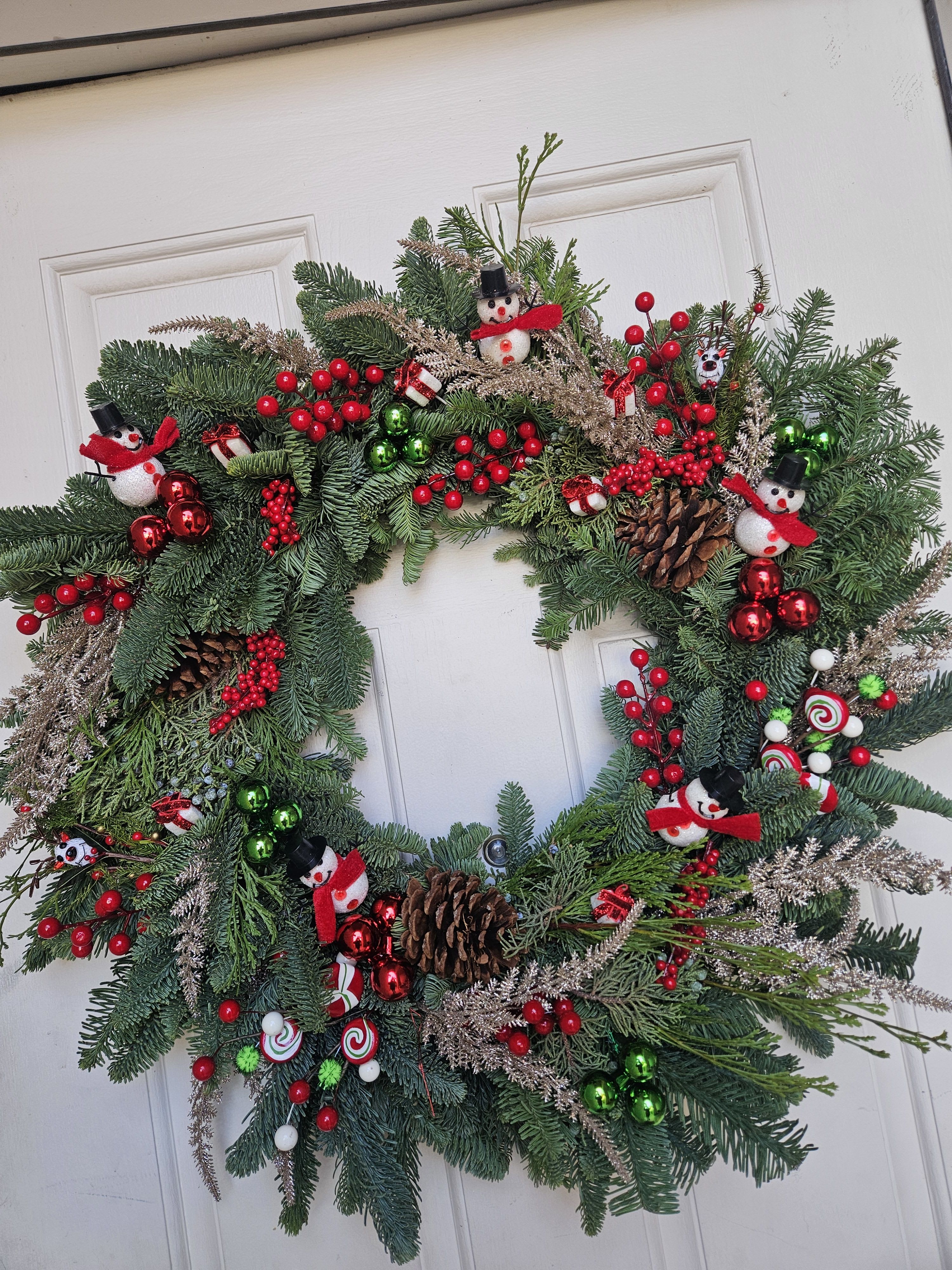 Christmas wreath with pine branches, red berries, pinecones, and snowman ornaments