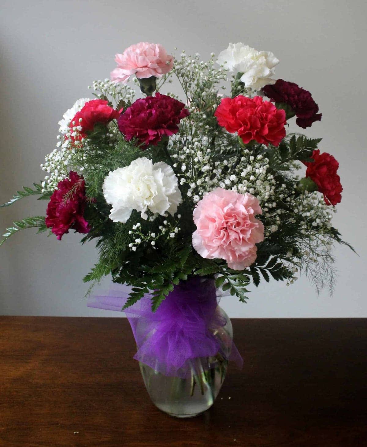 Dozen Mixed Carnations - 12 assorted colored carnations perfectly arranged in a glass vase with babies breath and premium greens. 
