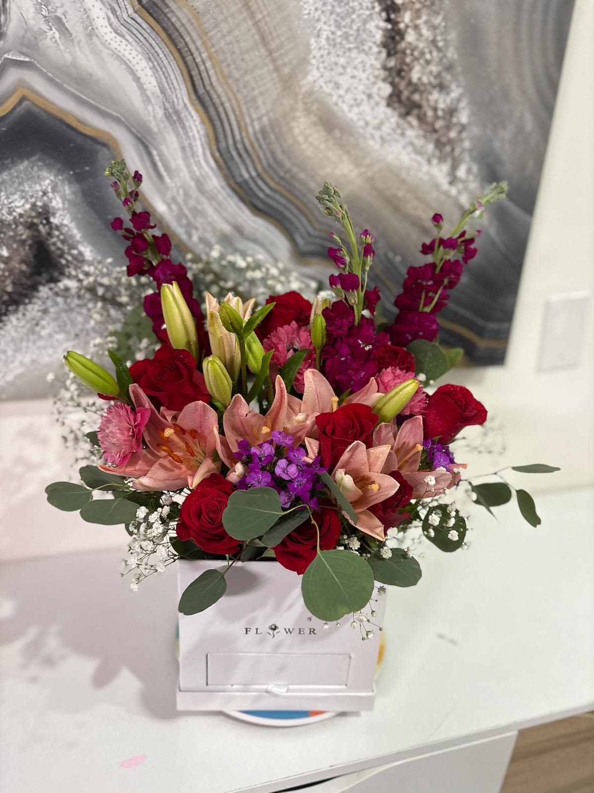 Mixed bouquet of red roses, pink lilies, and purple flowers in a white box