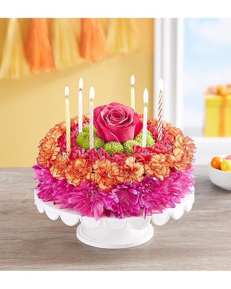 BIRTHDAY WISHES FLOWER CAKE VIBRANT - If you want their birthday to be the brightest day of the year, your wish has come true! Our vibrant new flower cake has all the ingredients for a happy celebration: hot pink and fiery orange blooms—and candles to top it off. This confection-inspired creation is the perfect centerpiece for their party. Dial up the fun by adding a balloon to your gift. ****** VASE PLATE WILL VARY ****** 