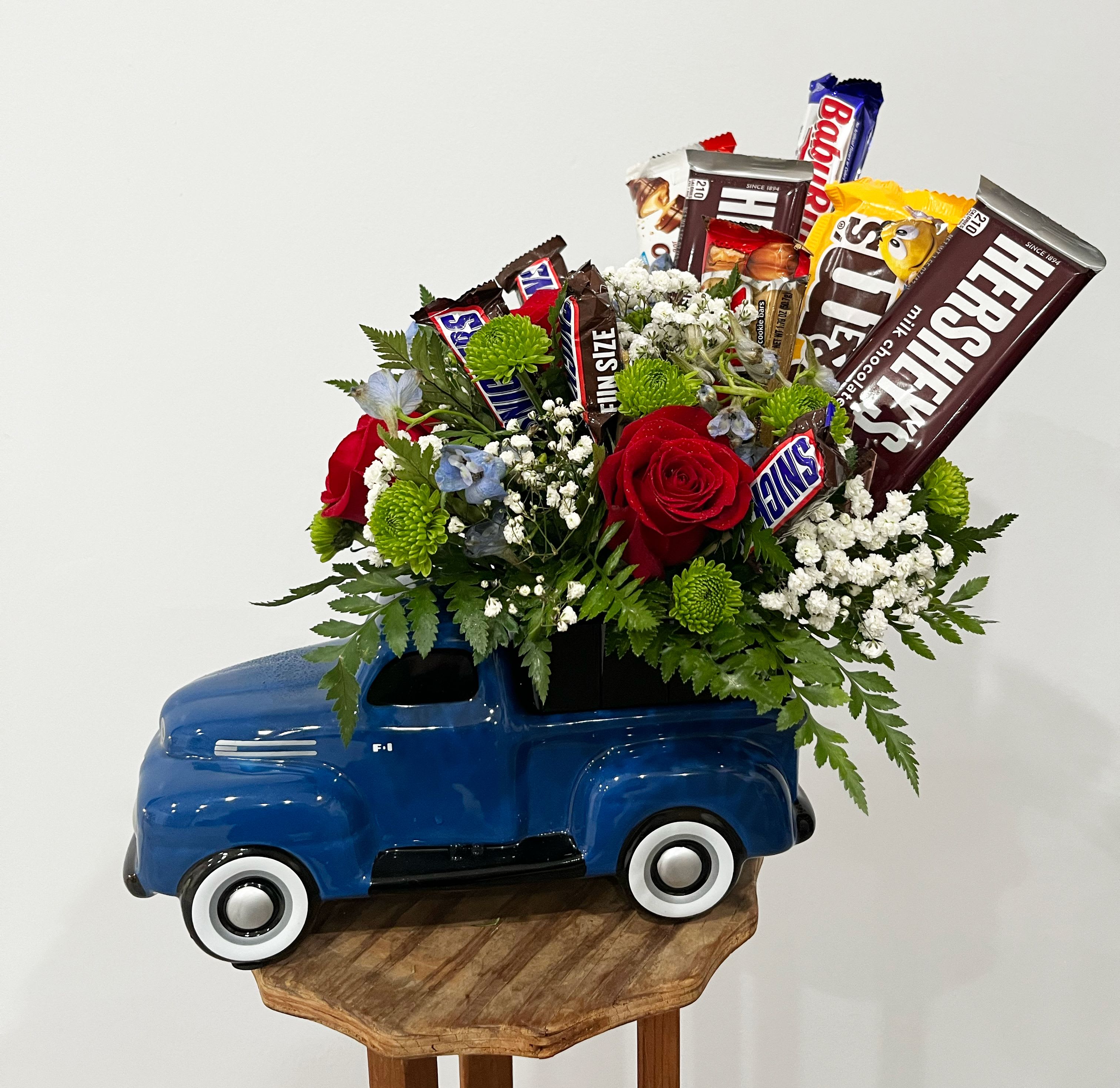 Sweet Ride Chocolate &amp; Floral Arrangement - Treat your loved ones to the perfect combination of elegance and indulgence with our Sweet Ride Chocolate &amp; Floral Arrangement! This unique gift features a charming ceramic blue vintage truck overflowing with a stunning mix of fresh red roses, green poms, blue delphinium and delicate baby's breath, and lush greenery. To top it off, an assortment of popular chocolate bars—including Hershey's, Snickers, and Baby Ruth—adds a delightful sweet touch. Whether you're celebrating a birthday, Father's Day, or just want to brighten someone's day, this creative and thoughtful arrangement is sure to impress!    Perfect for: Birthdays, Anniversaries, Father’s Day, Thank You Gifts, or Just Because!  Includes: Fresh flowers, assorted chocolates, and a keepsake blue ceramic truck.