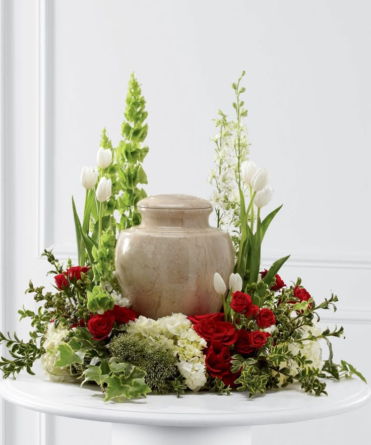 Circle of Remembrance Cremation Tribute - Celebrate a life well-lived with our "Circle of Remembrance Cremation Tribute" a handcrafted floral ring designed to encircle a cremation urn or framed photograph. This elegant arrangement features a harmonious blend of soft pink roses, delicate white lilies, soothing lavender chrysanthemums, and verdant eucalyptus, symbolizing love, purity, and remembrance. Accented with seasonal greenery and subtle fillers, the wreath offers a serene and heartfelt tribute, perfect for memorial services, celebrations of life, or as a lasting homage at home.​