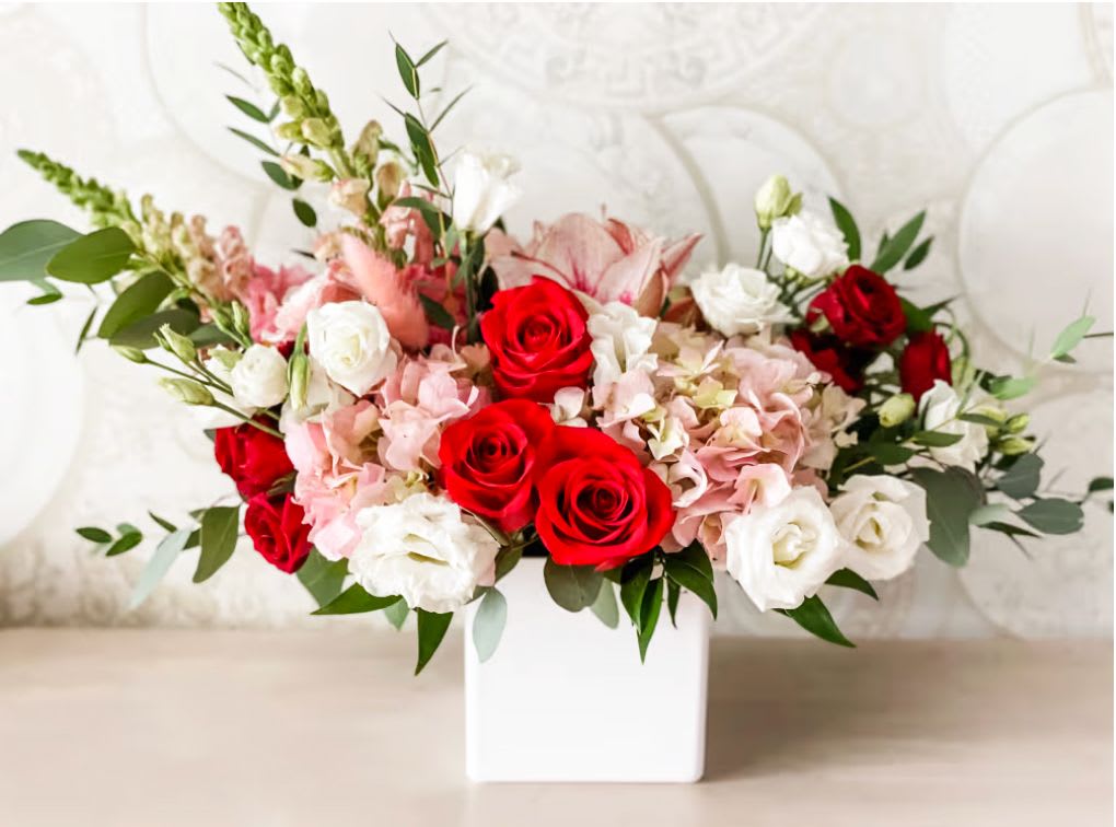 Love Blooms - An enchanting expression of romance and grace. Love Blooms features a luxurious mix of red roses, white lisianthus, pink hydrangeas, and delicate snapdragons, all nestled in a sleek white box vase. With soft greenery to complement its rich blooms, this arrangement is perfect for anniversaries, Valentine's Day, or to say “I love you” in the most elegant way.