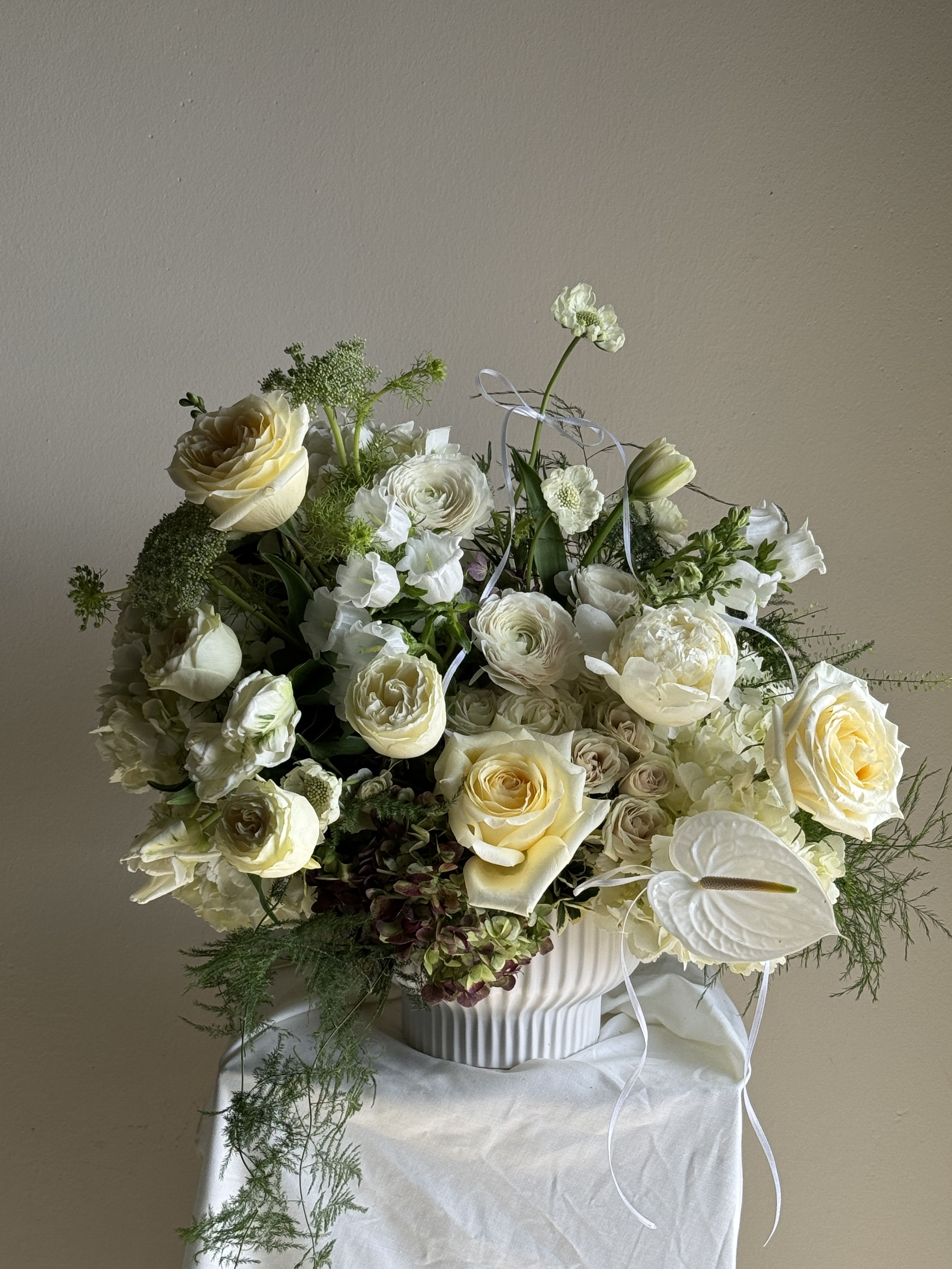 Cream and white floral arrangement in a ribbed white vase with ribbon accents