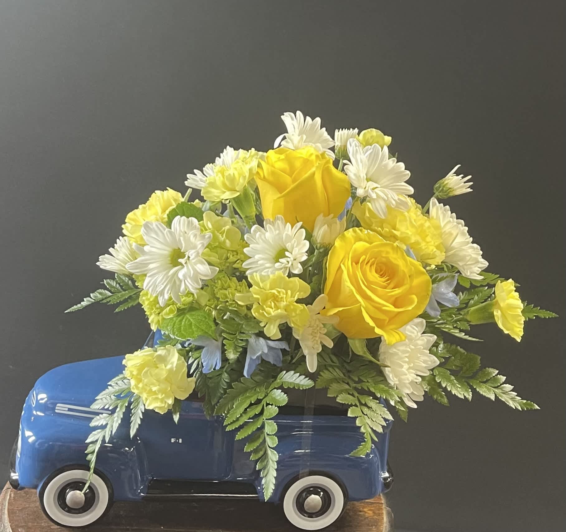Yellow roses and white daisies arranged in a blue toy truck