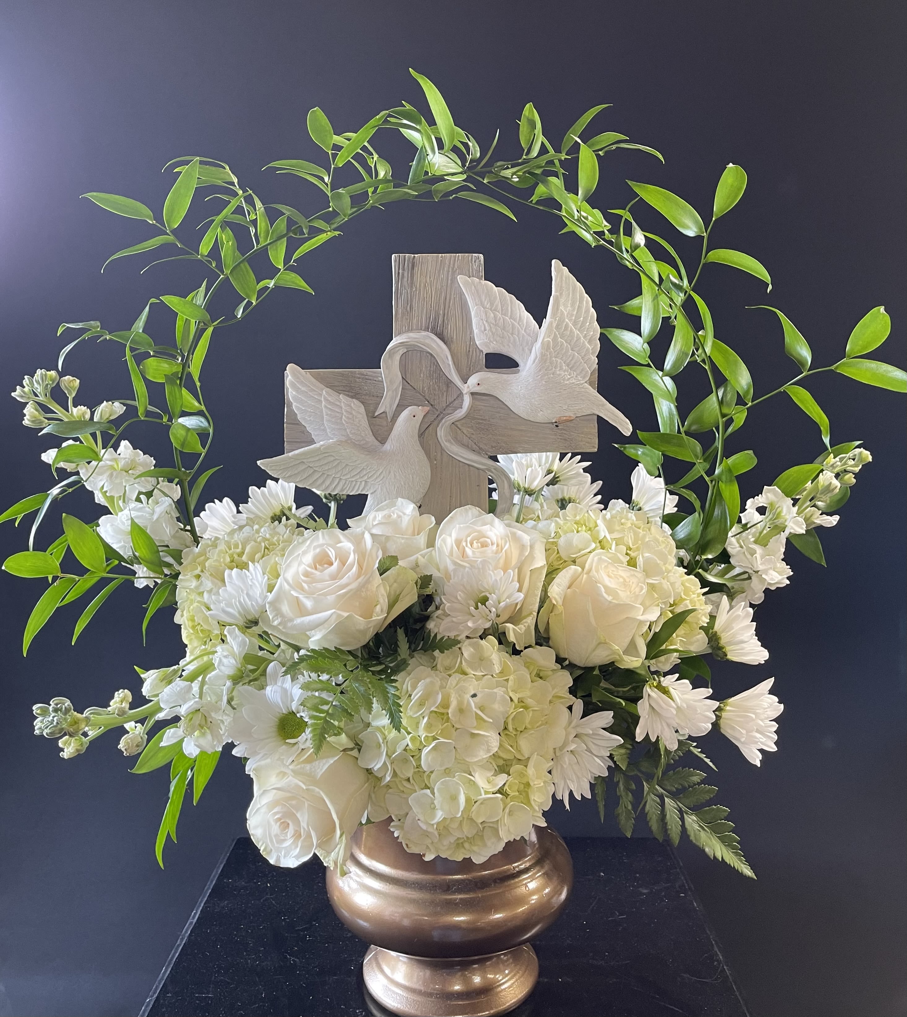 White floral arrangement with roses, hydrangeas, and a cross topper