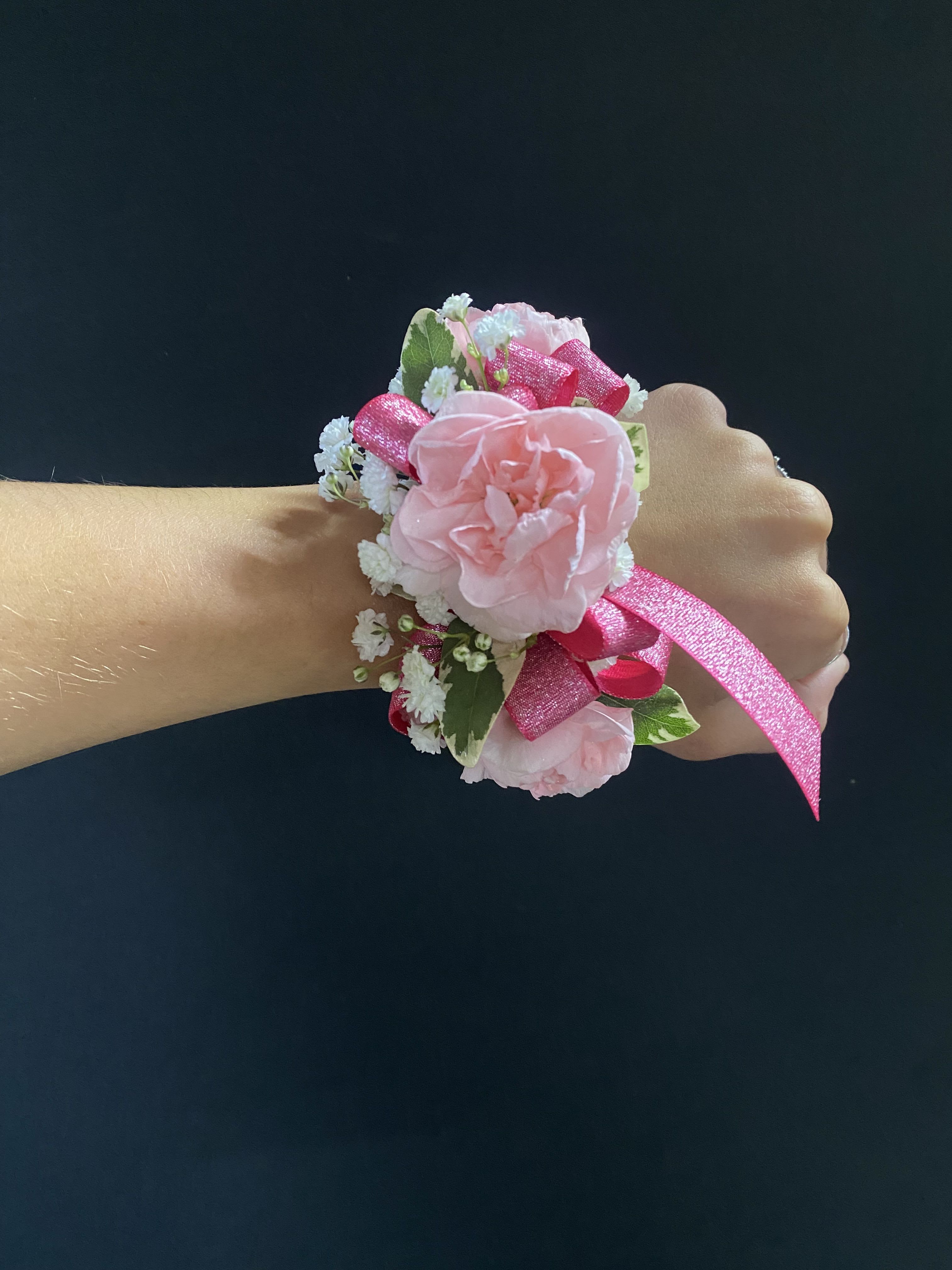 Pink floral wrist corsage with ribbon on a person's wrist