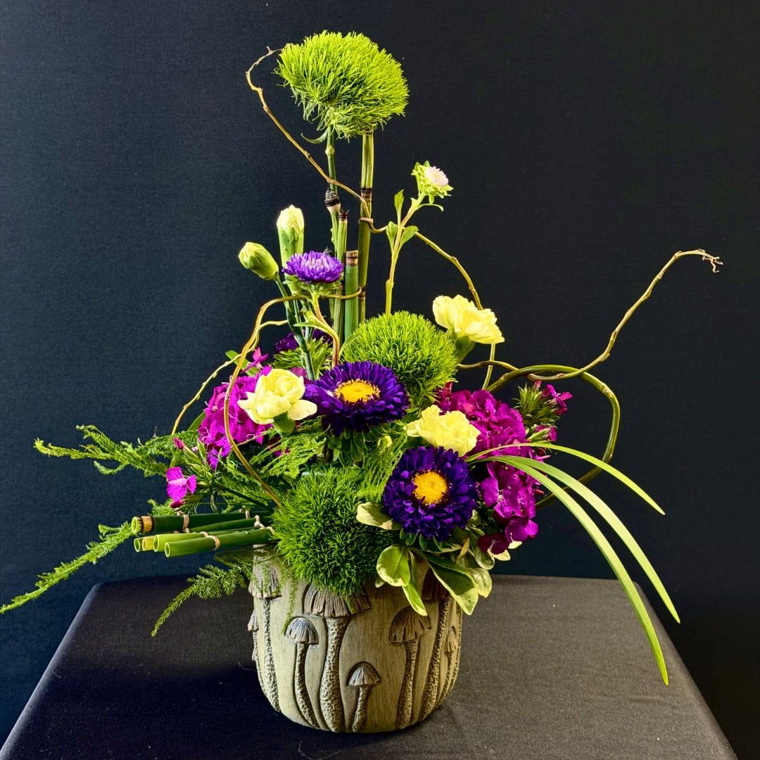 Tall floral arrangement with purple and yellow blooms in a mushroom-textured vase