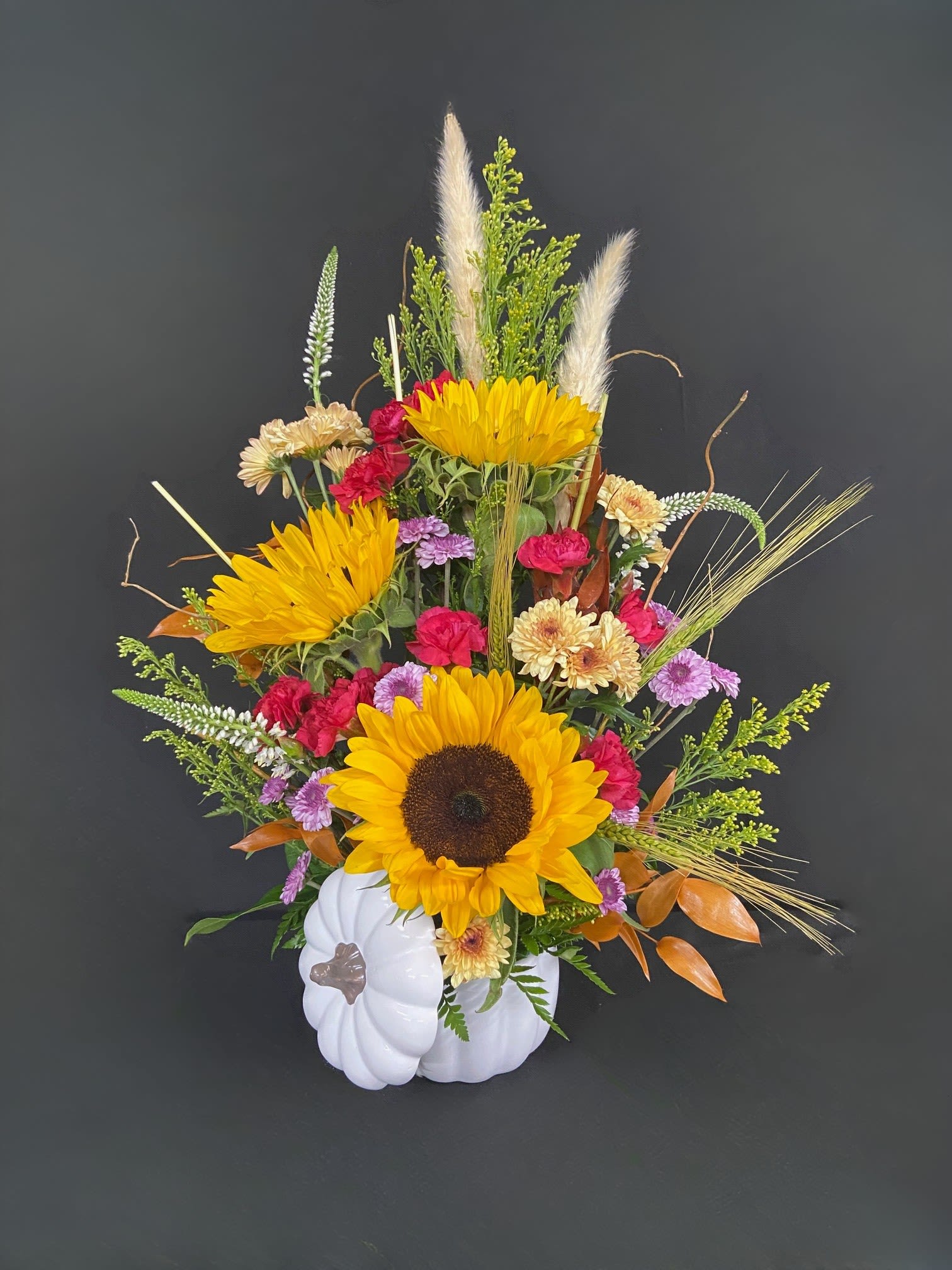 Sunflower arrangement in a white pumpkin container with mixed blooms and grasses