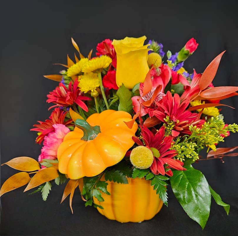 Colorful fall bouquet in a pumpkin-shaped container with red, yellow, and orange flowers