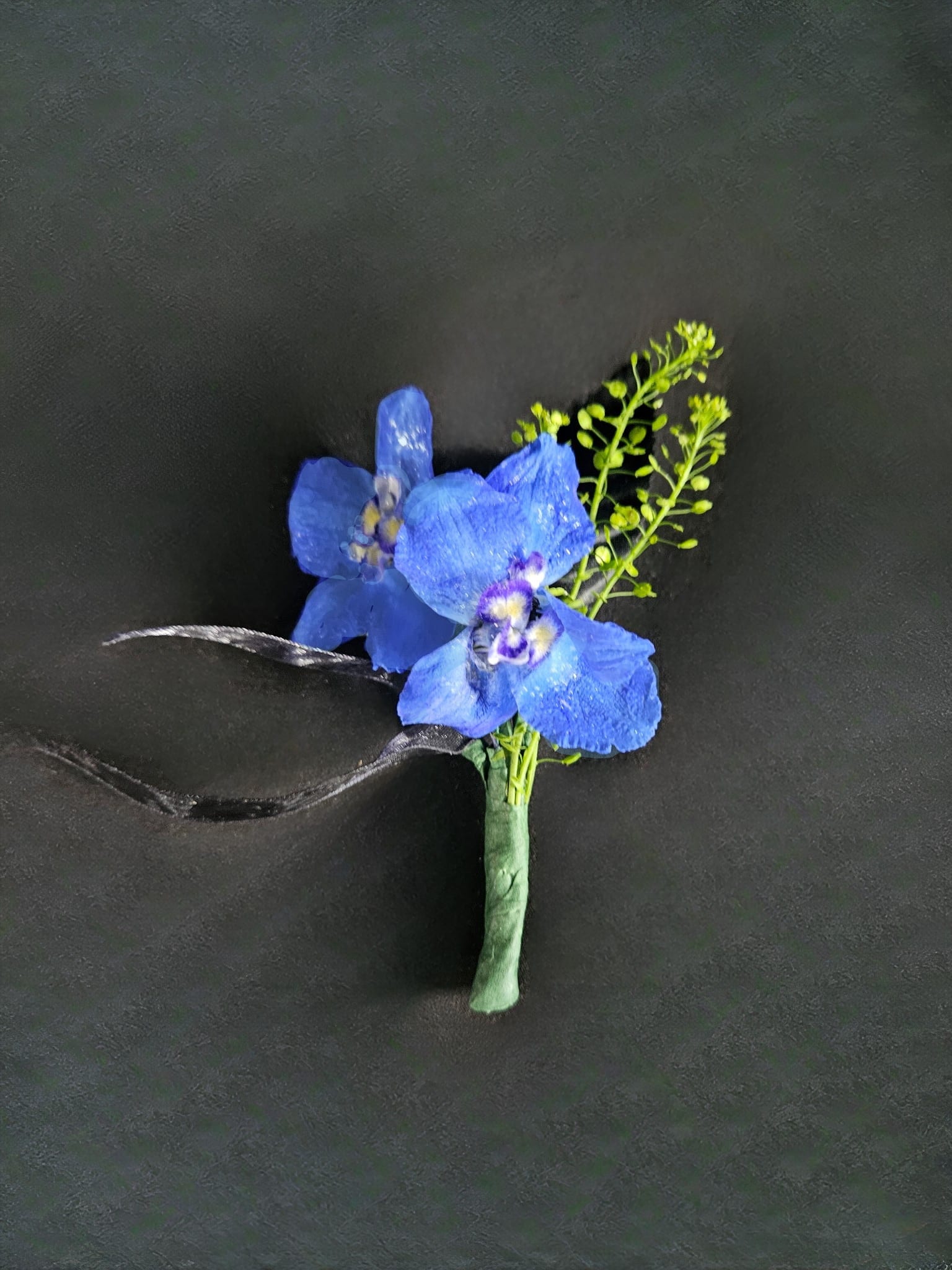 Light Blue Delphinium Boutonniere - A naturally blue flower that will compliment any outfit. The only flower color option for this boutonniere is light blue. Please select up to 2 ribbon colors from the add-on selections you would like included. (Please do not select any of the flower color options)