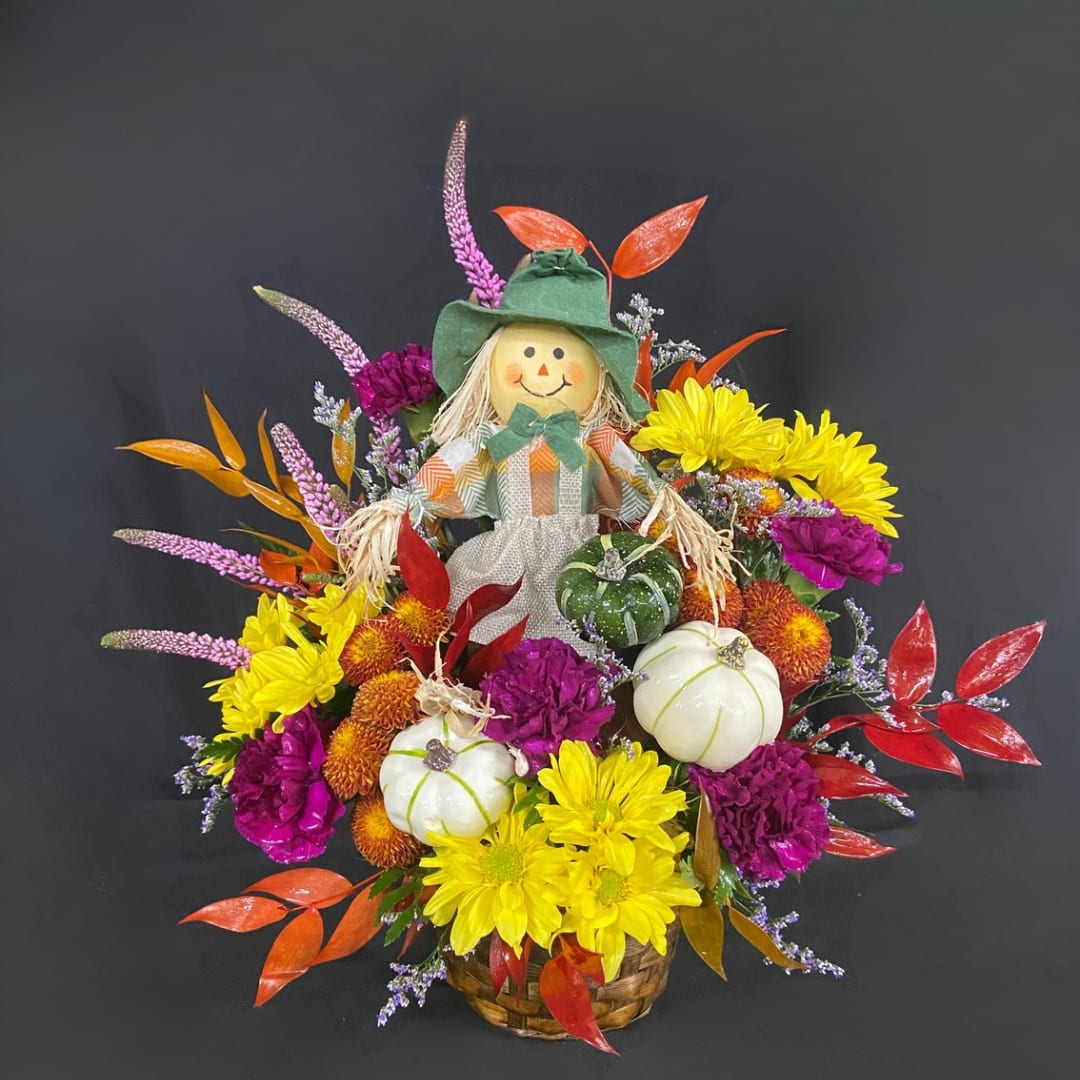 Fall floral basket with a scarecrow figure, pumpkins, and bright mums