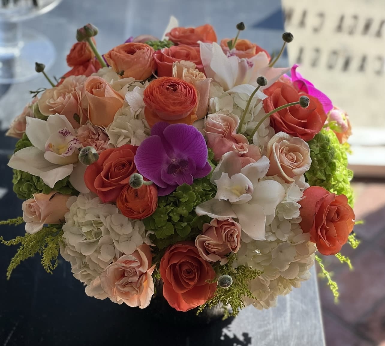 Round bouquet of coral and white flowers with a purple orchid accent