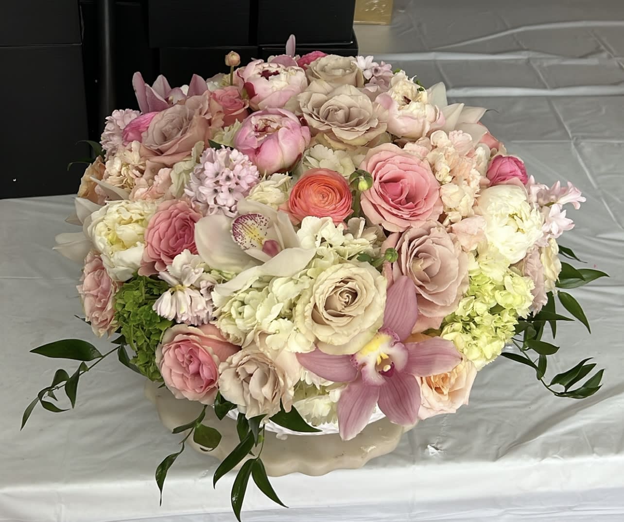 Large pastel bouquet of roses, orchids, and hydrangeas in a low vase