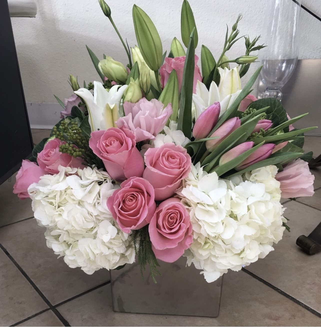 Pink roses and white lilies in a square glass vase with white hydrangeas