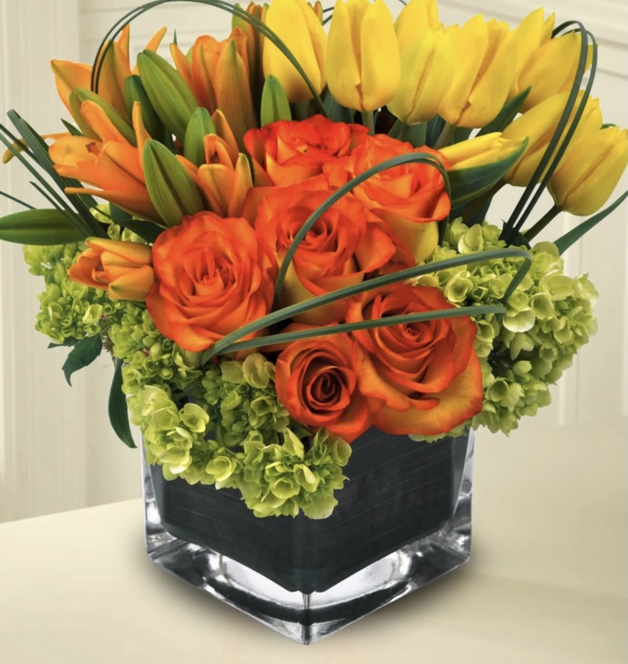 Orange roses and yellow tulips arranged in a square glass vase