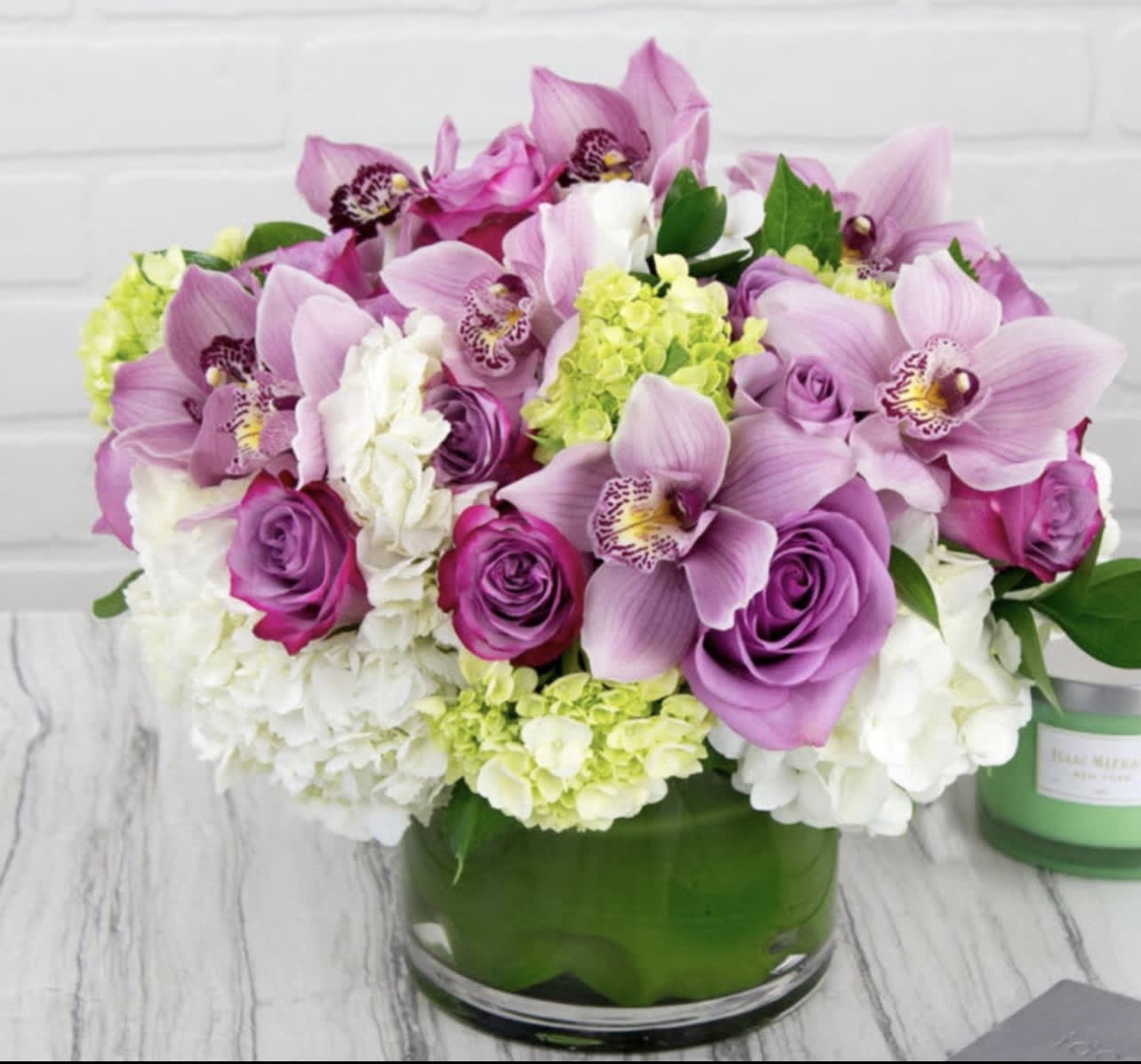 Pink orchids and roses arranged in a green glass vase