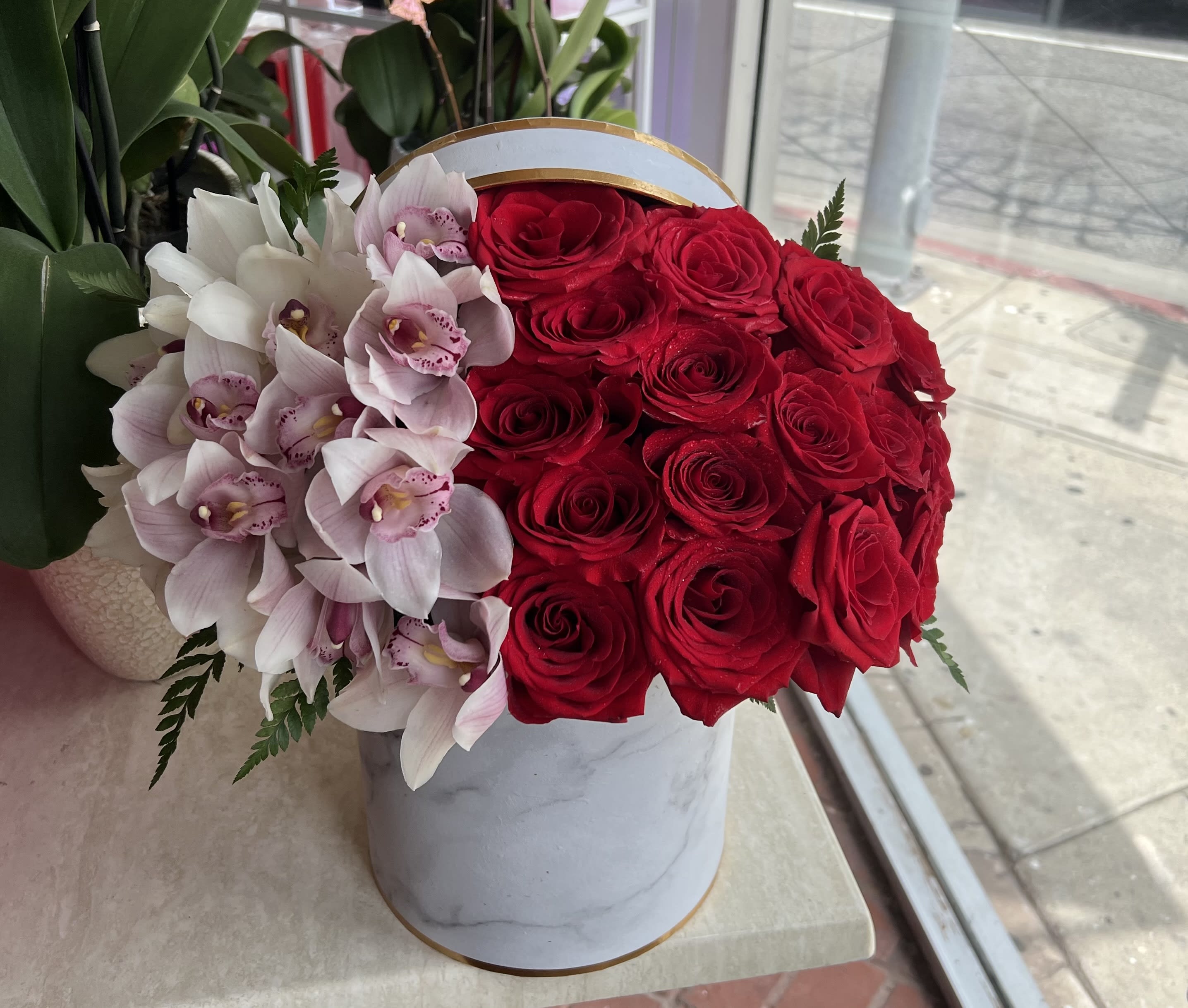 Red roses and pale pink orchids in a white round box