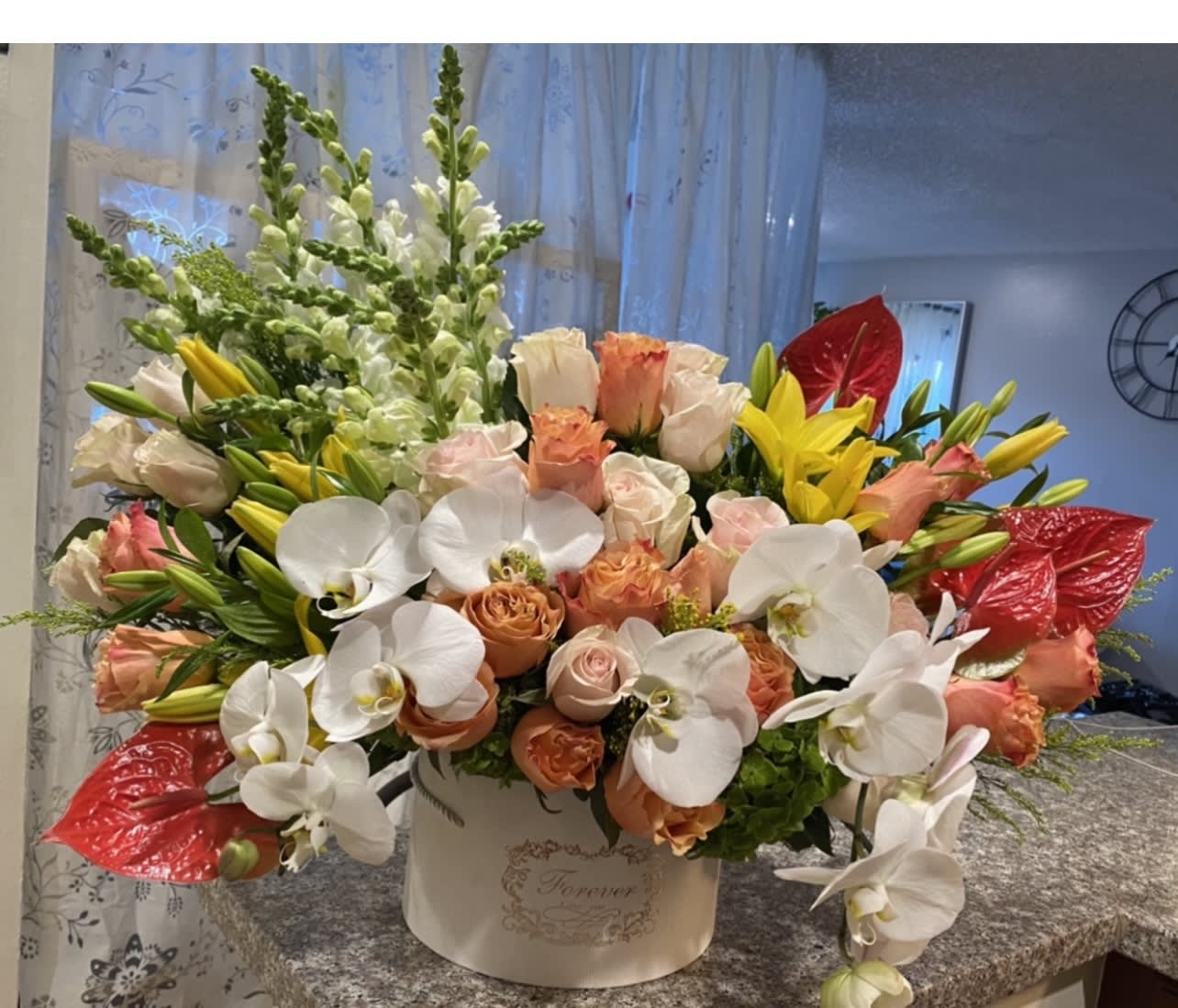 Mixed bouquet of white orchids, peach roses, yellow lilies, and red anthuriums in a white box