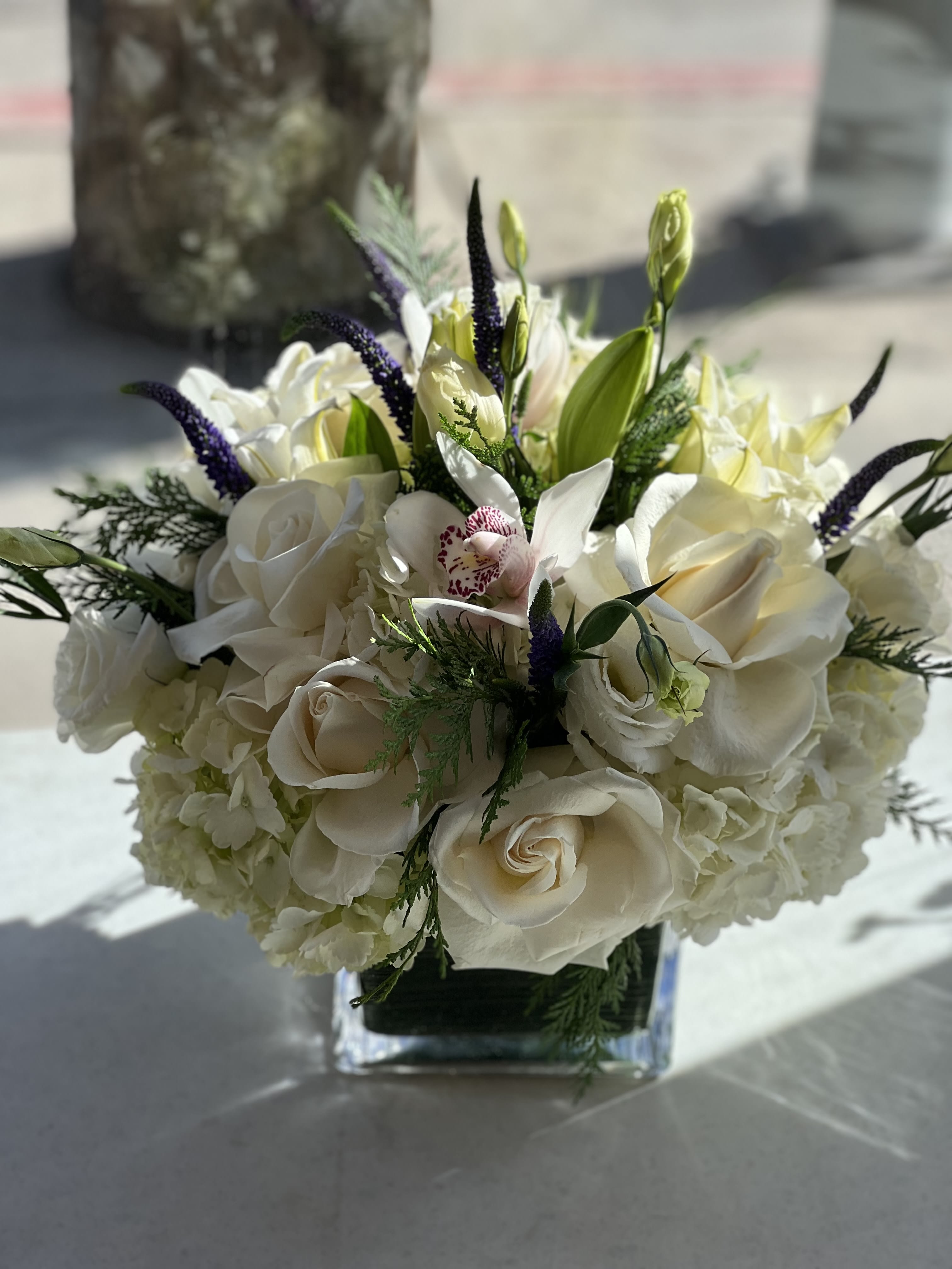 White rose and orchid bouquet in a square glass vase