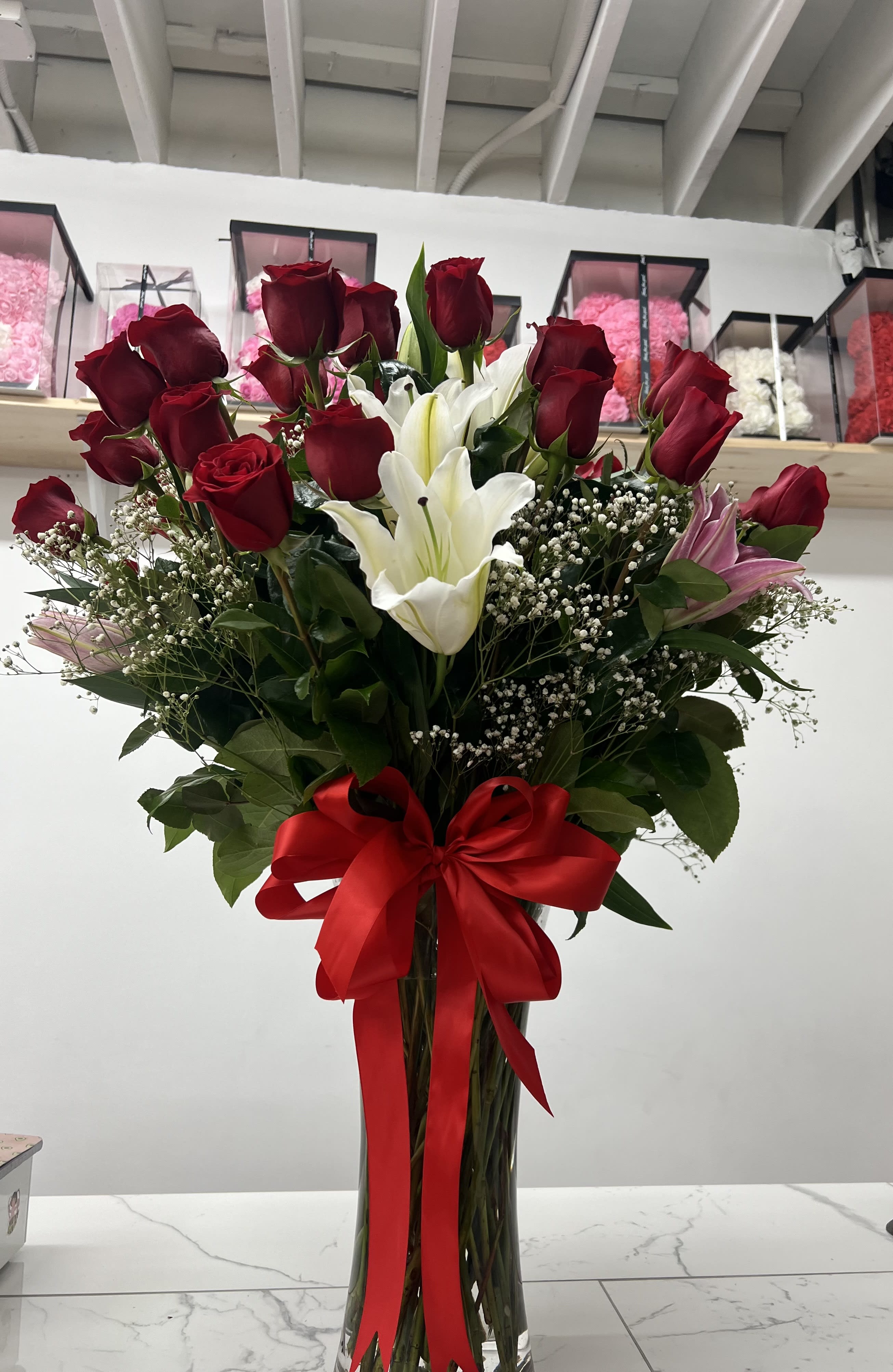 Tall bouquet of red roses and white lilies in a glass vase with a red ribbon