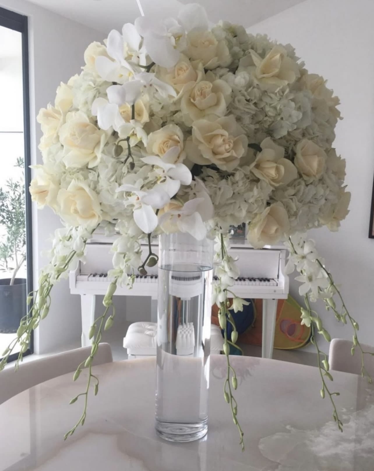 White floral arrangement in a clear glass vase with trailing orchids