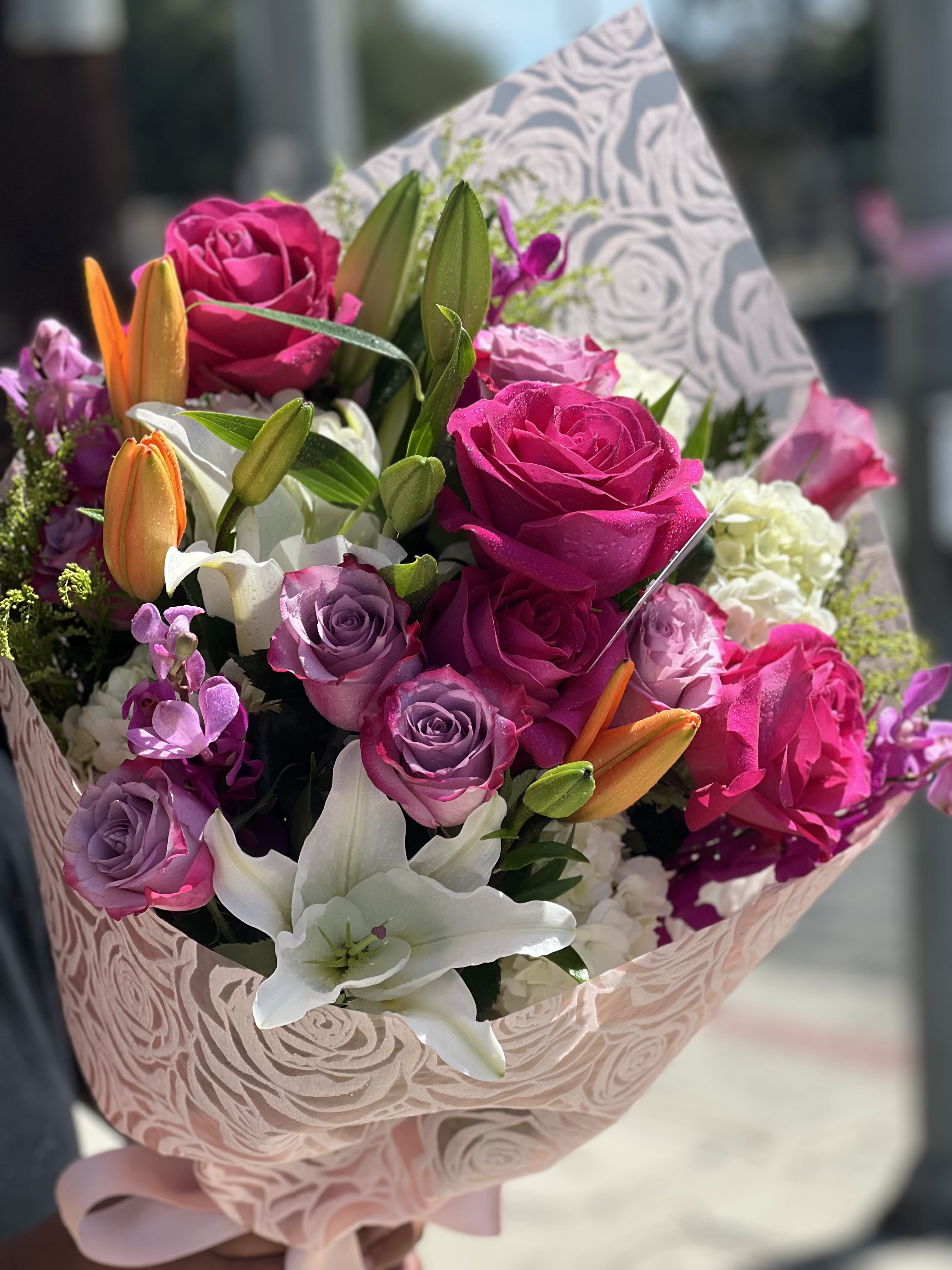 Bouquet of pink and purple roses with white lilies and orange buds