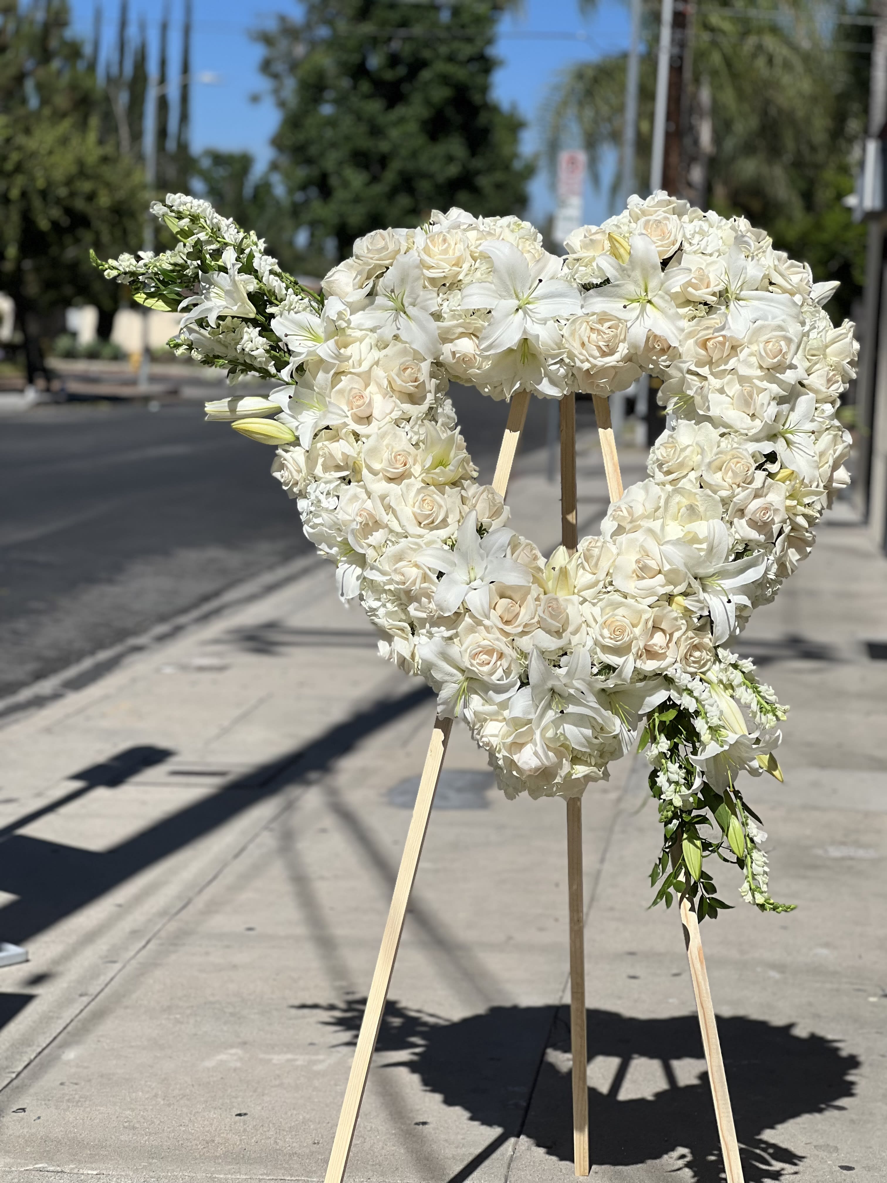 Heart-shaped white floral wreath on a wooden stand outdoors