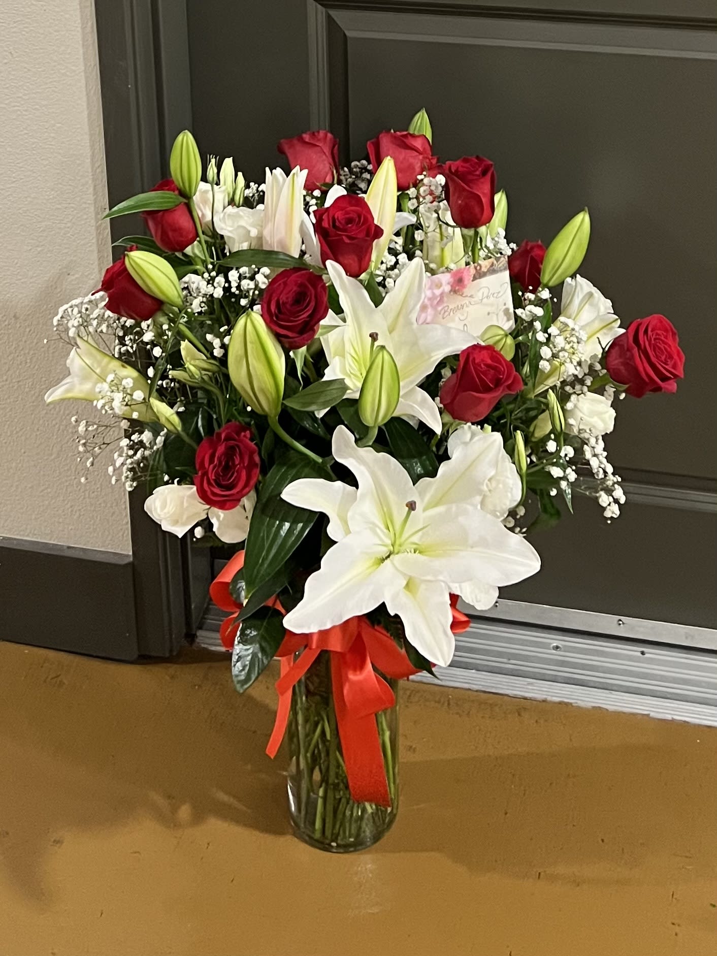 Bouquet of red roses and white lilies in a glass vase with a red ribbon