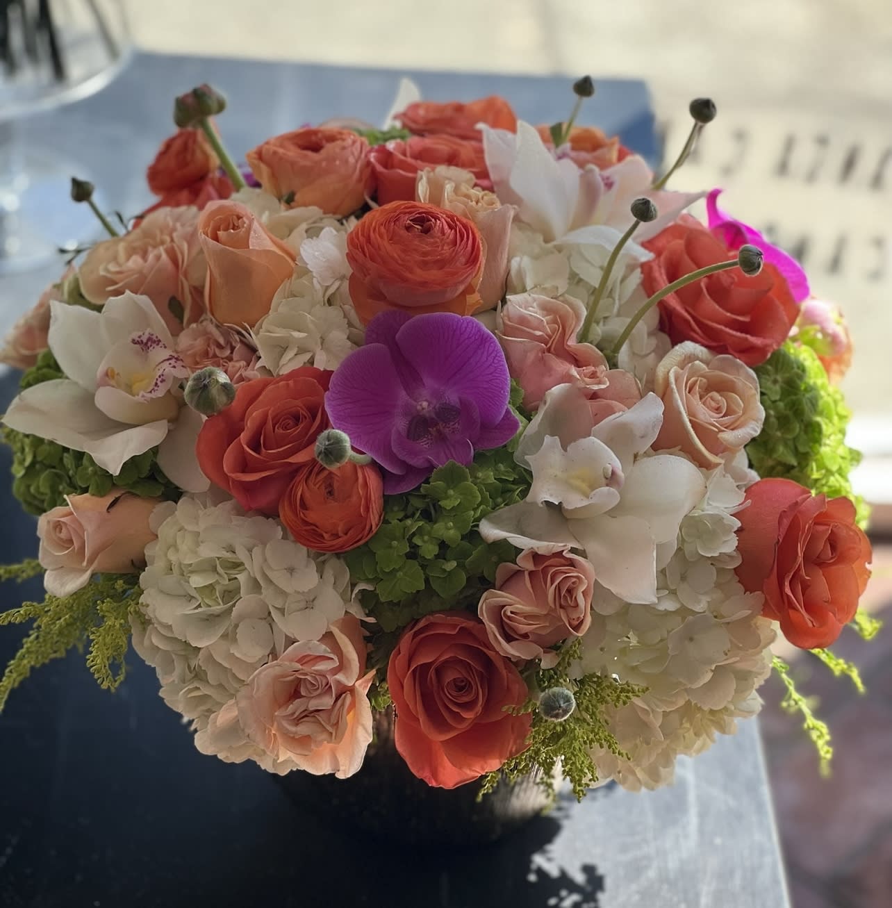 Round bouquet of coral and blush roses with white orchids and hydrangeas