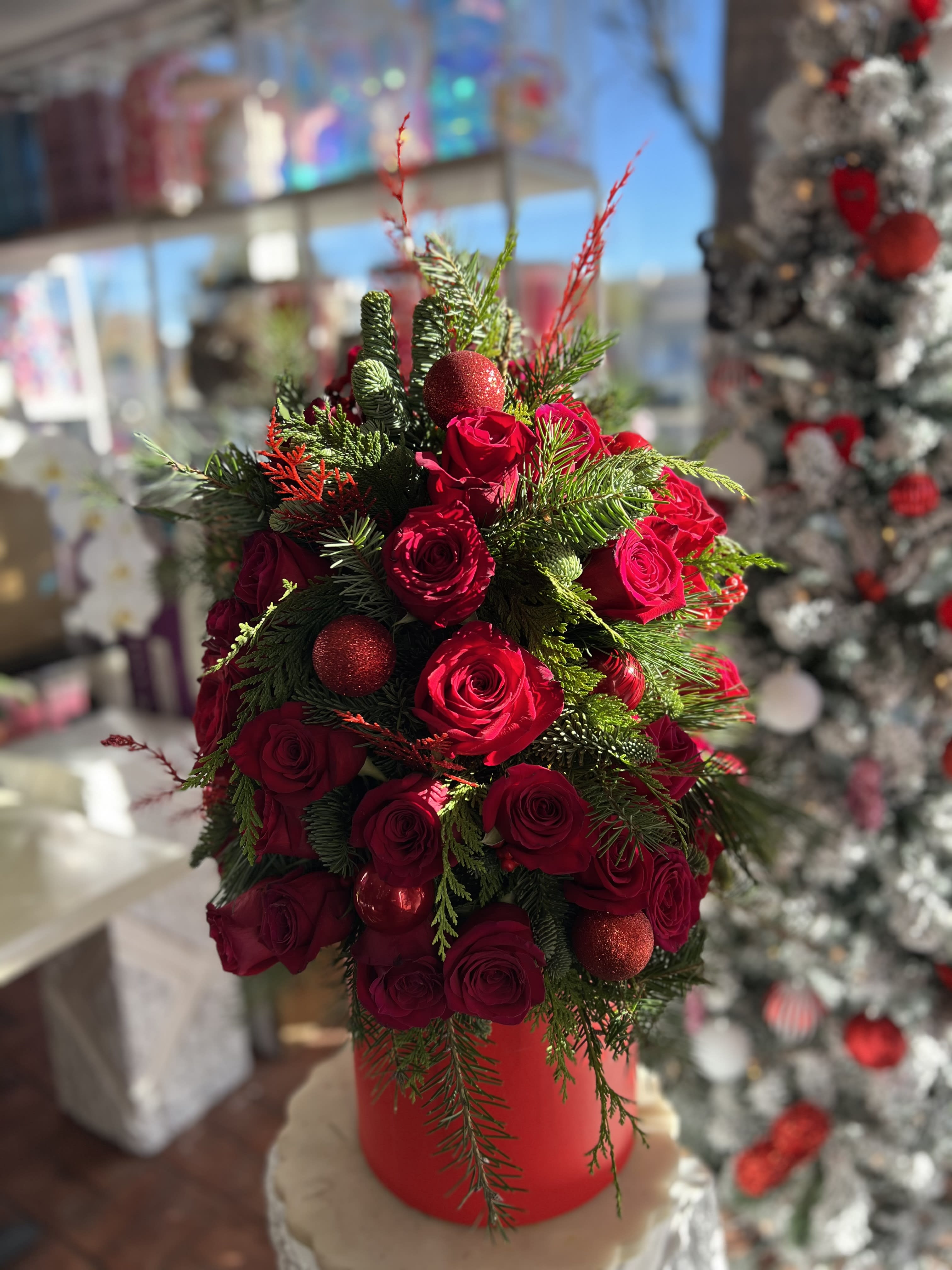 Red roses arranged with evergreen and red ornaments in a red container