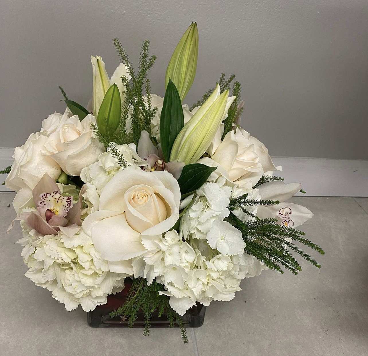 White roses and lilies arranged in a low square vase