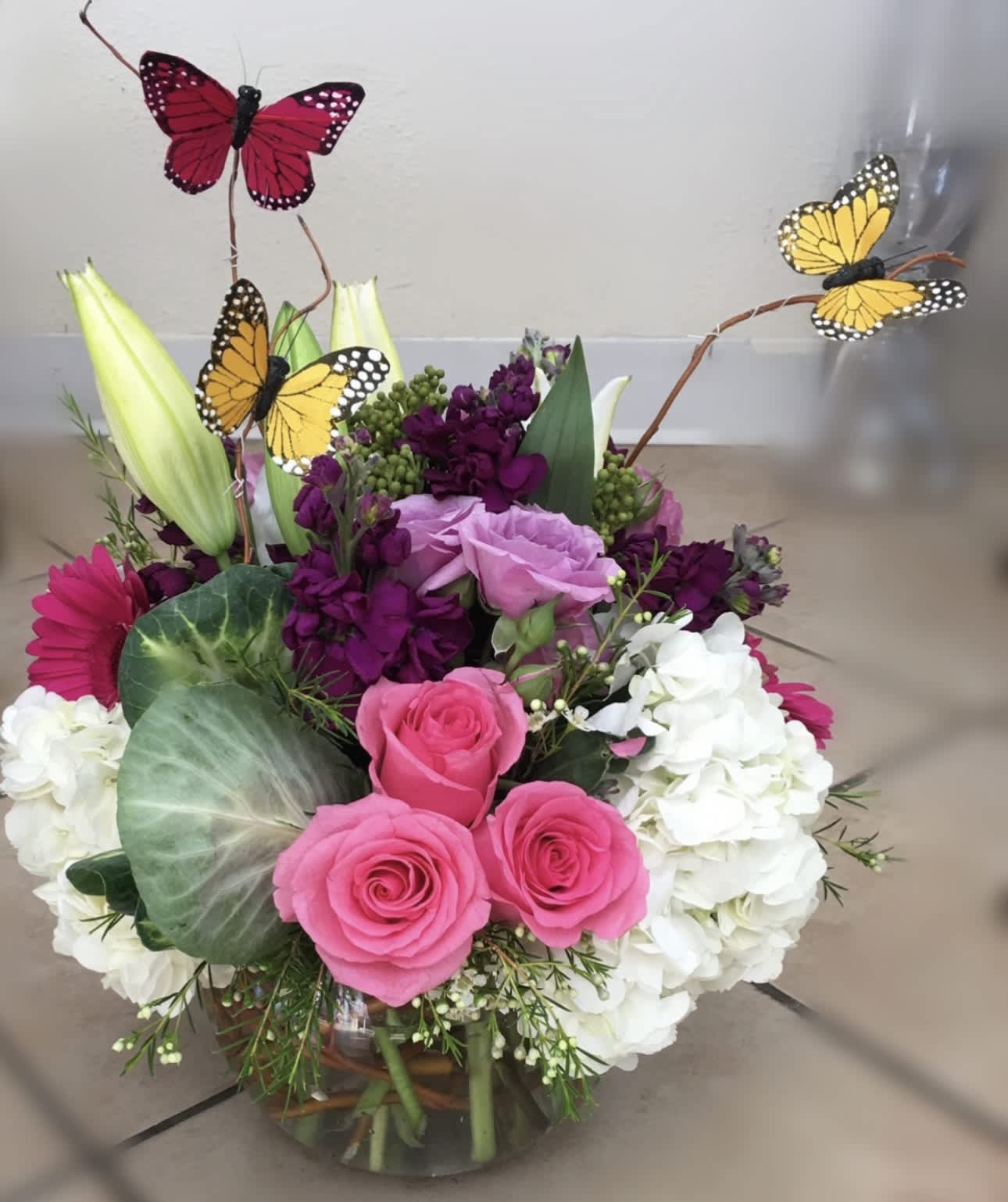 Pink roses and white hydrangeas with butterfly picks in a glass vase