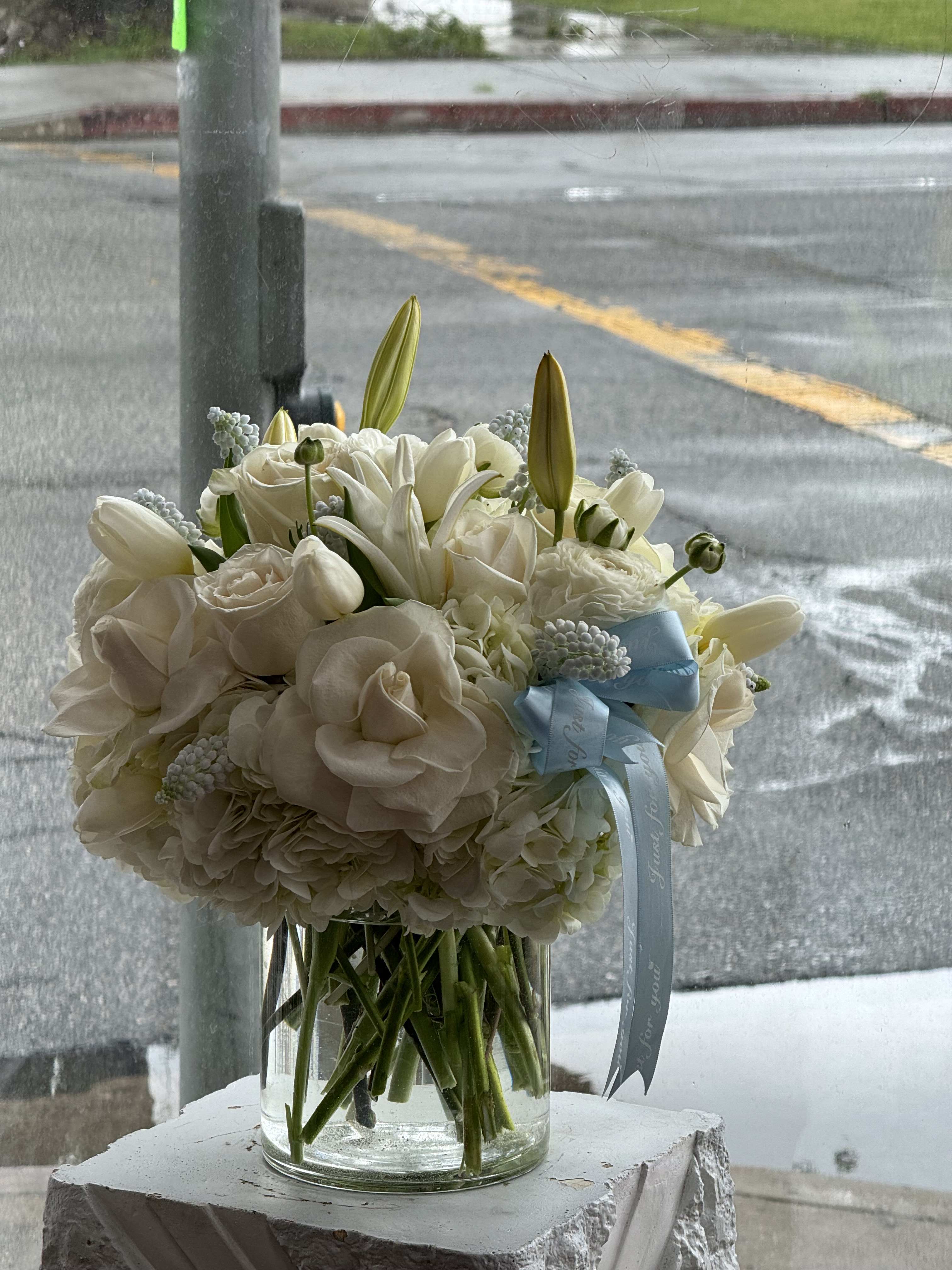 White bouquet in a clear glass vase with a blue ribbon