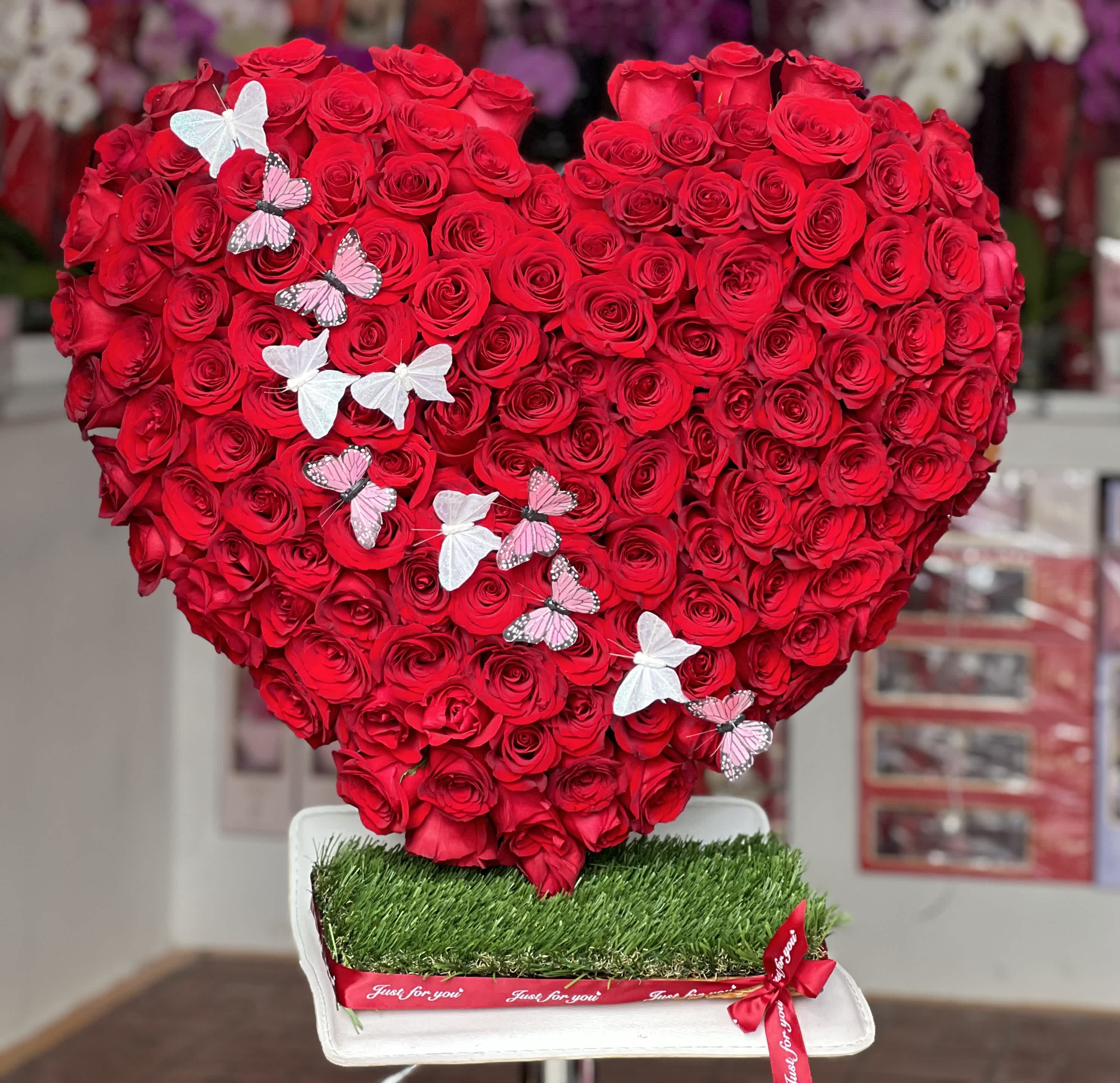 Heart-shaped arrangement of red roses with butterfly decorations on a white base