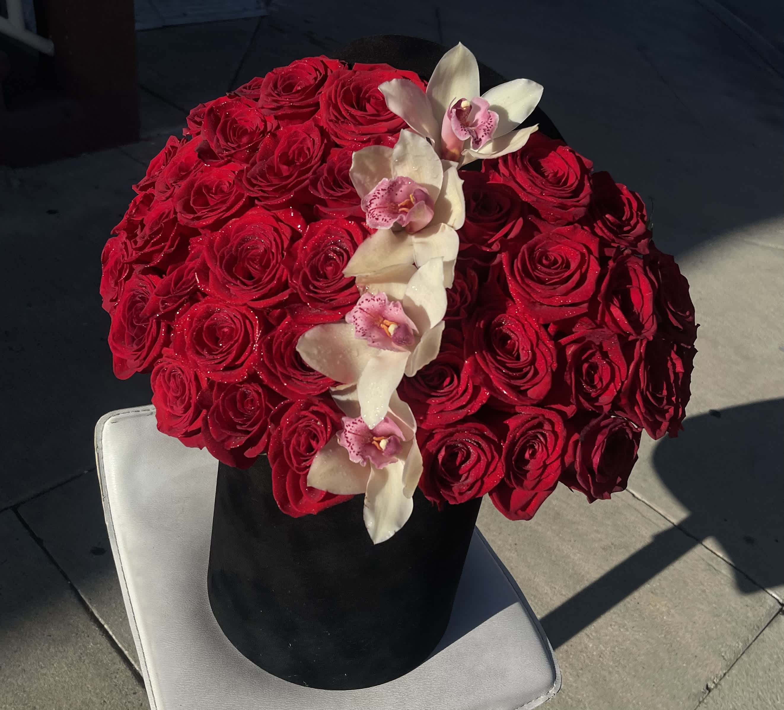 Red rose arrangement with white orchids in a black hatbox