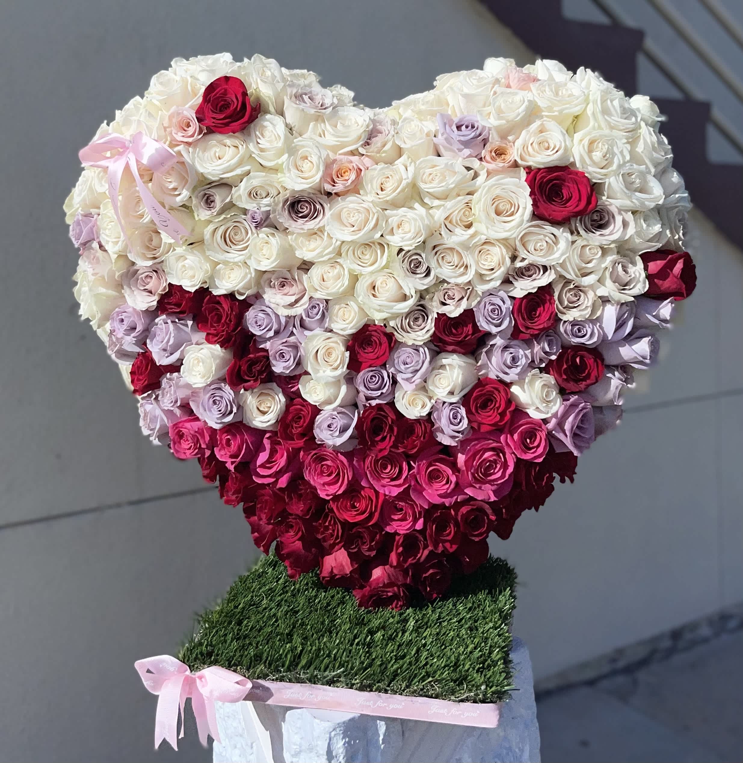 Heart-shaped rose arrangement in white, pink, and red with a pink ribbon