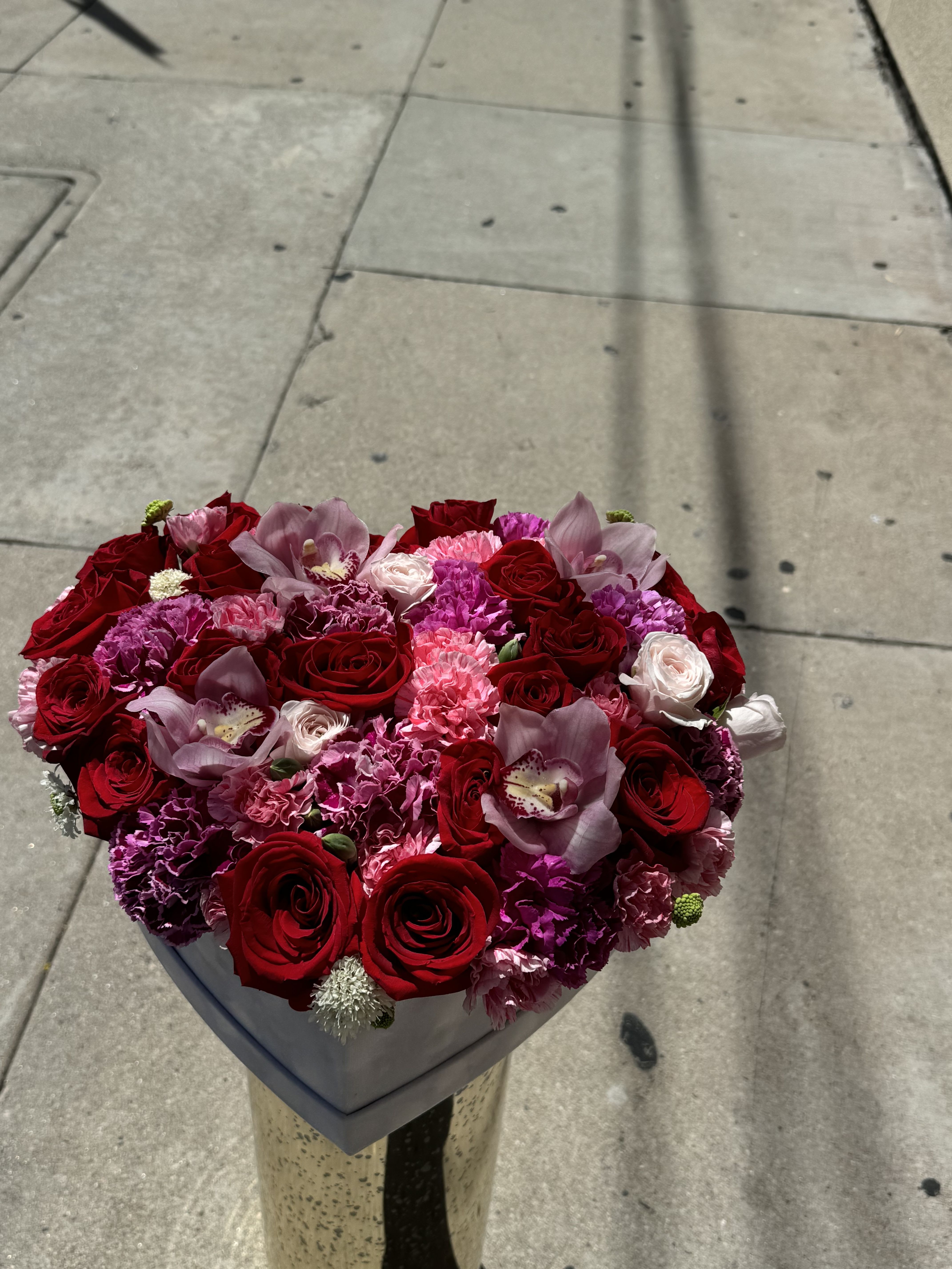 Heart-shaped bouquet of red roses, pink carnations, and orchids